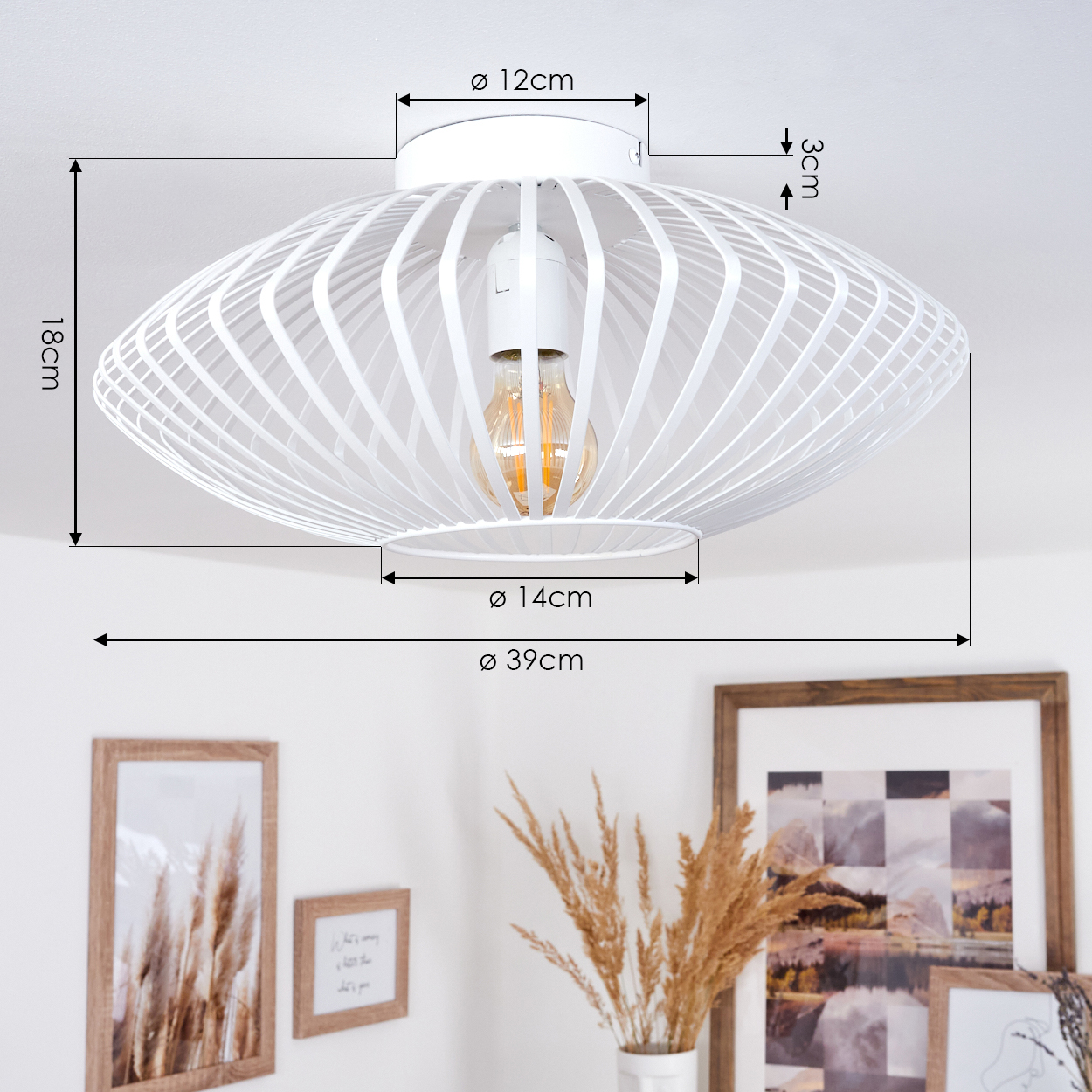 Weiße, geometrische Deckenlampe mit sichtbarer Glühbirne. Darunter gerahmte Bilder und eine Vase mit getrockneten Pflanzen.