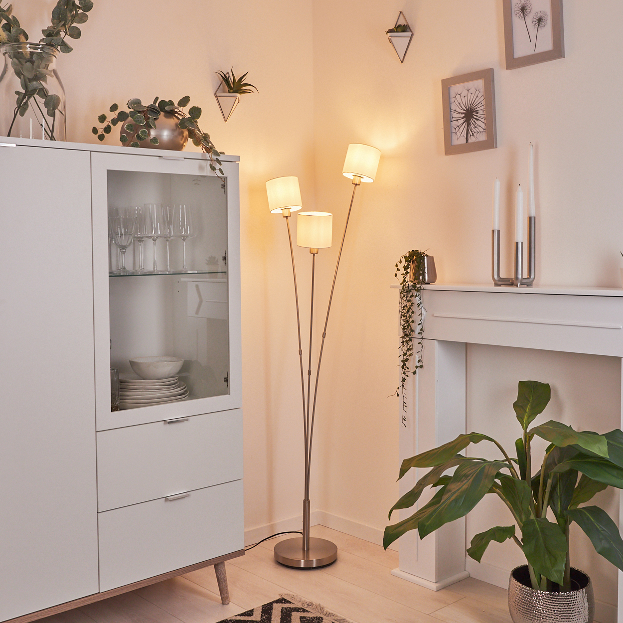 Ein modernes Wohnzimmer mit Stehlampe, weißem Schrank und Pflanzen. Weiches Licht erfüllt den Raum, die Einrichtung ist minimalistisch.