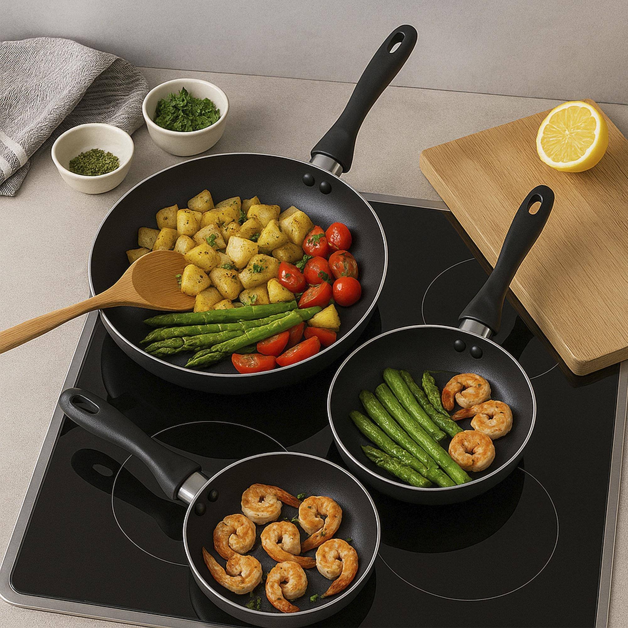 Sartenes con comida en una estufa. Se ven patatas, tomates, espárragos y camarones. También hay limón y hierbas.