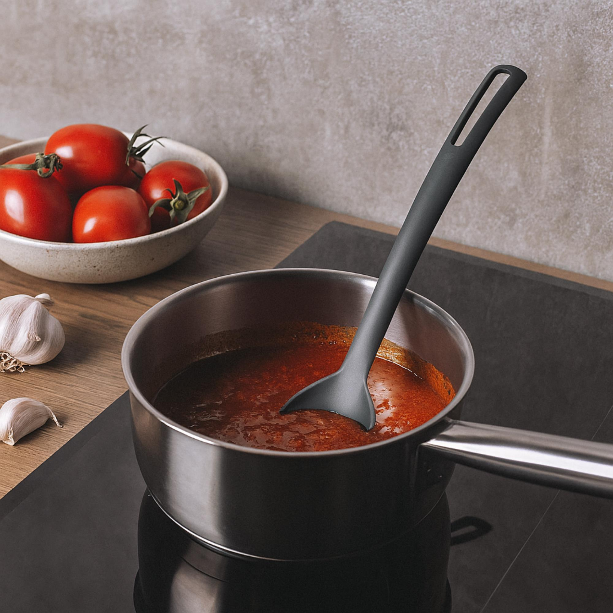 Una olla de salsa de tomate hierve a fuego lento en una estufa, con un cucharón. Tomates y ajo al lado.