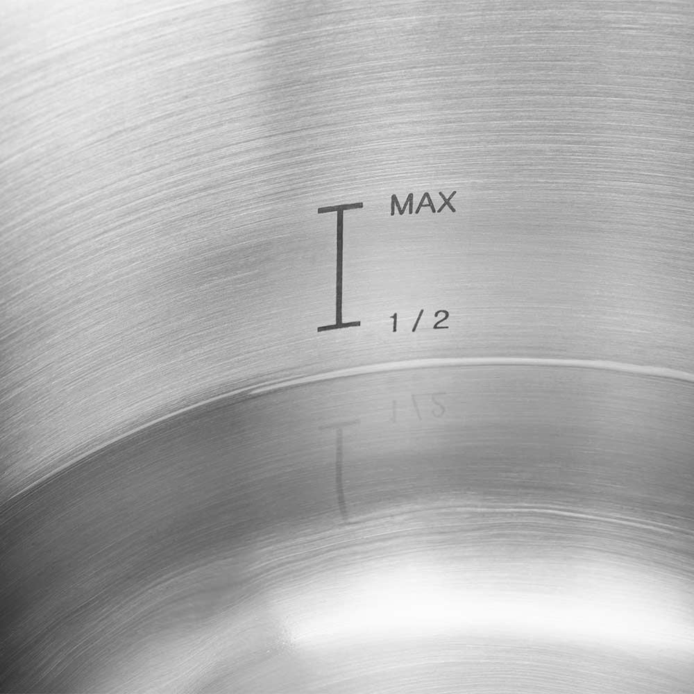 Zbliżenie wnętrza metalowego garnka ze wskaźnikami poziomu: 'I', 'MAX' i '1/2'. Powierzchnia ma koncentryczne wzory okręgów.