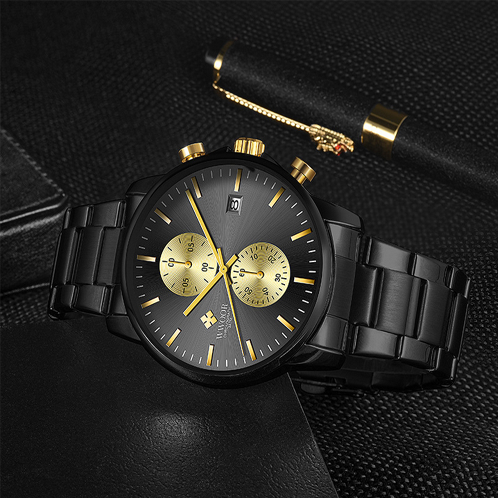 Schwarze Armbanduhr mit goldenen Akzenten auf dunkler Oberfläche, neben einem Stift. Die Uhr hat mehrere Zifferblätter und Datumsanzeige.