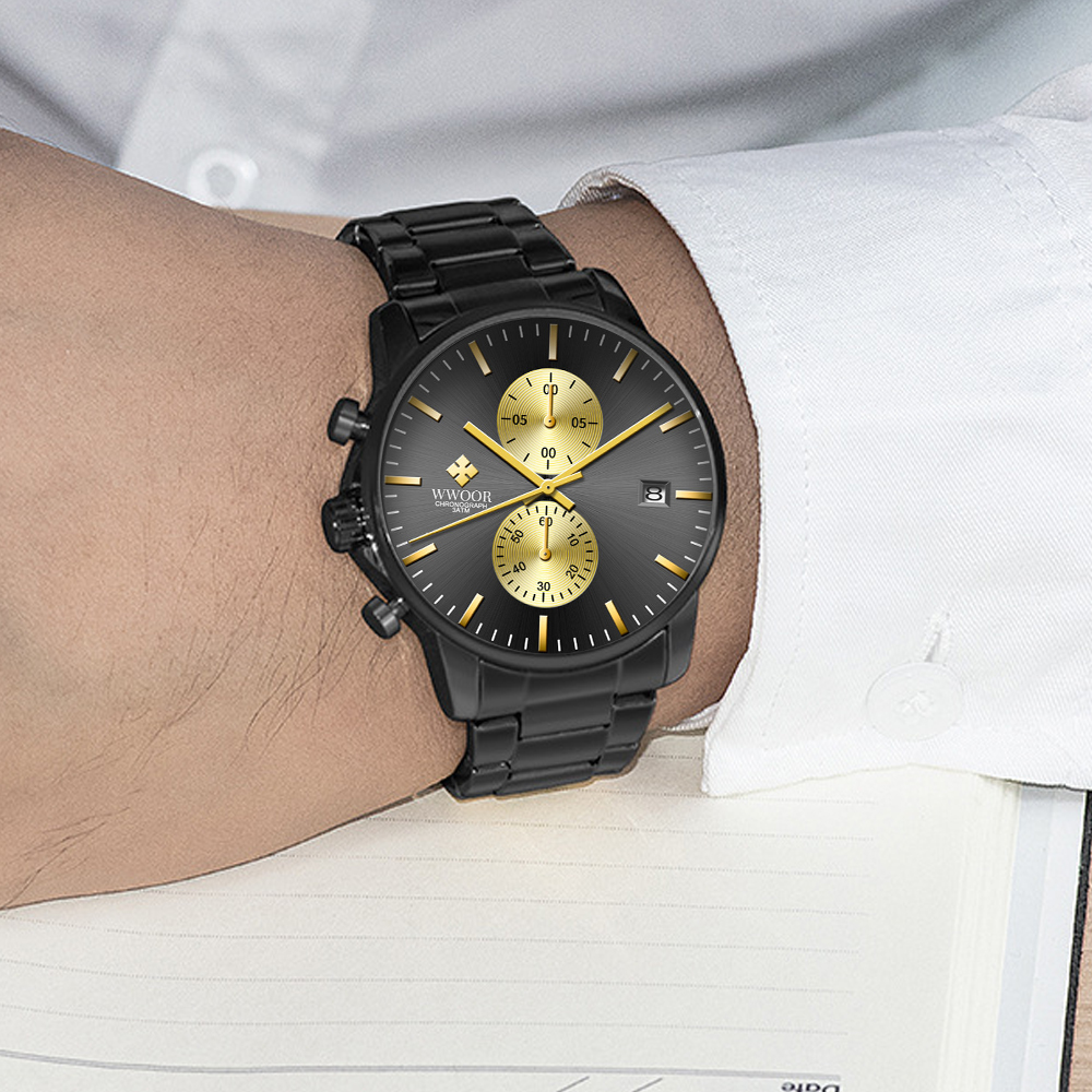 Schwarze Armbanduhr mit goldenen Akzenten an einem Handgelenk. Die Uhr hat drei Hilfszifferblätter und befindet sich an einem Handgelenk, das ein weißes Hemd trägt.