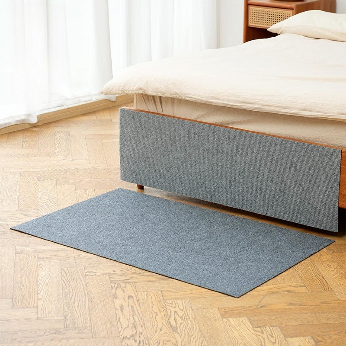 Schlafzimmer mit Bett, grauem Teppich und Holzboden. Das Bett hat eine beige Bettdecke. Ein Nachttisch ist im Hintergrund zu sehen.