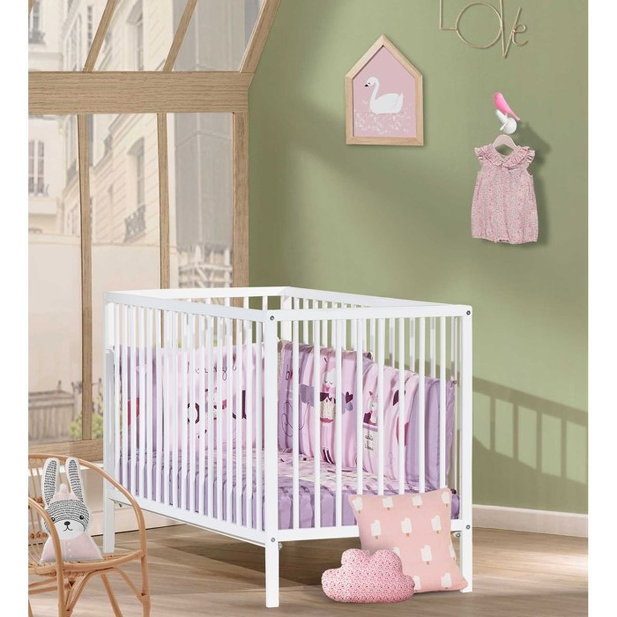 Una habitación para bebés con una cuna blanca llena de ropa de cama rosa. Una silla de conejito, obras de arte y un vestido cuelgan de la pared.
