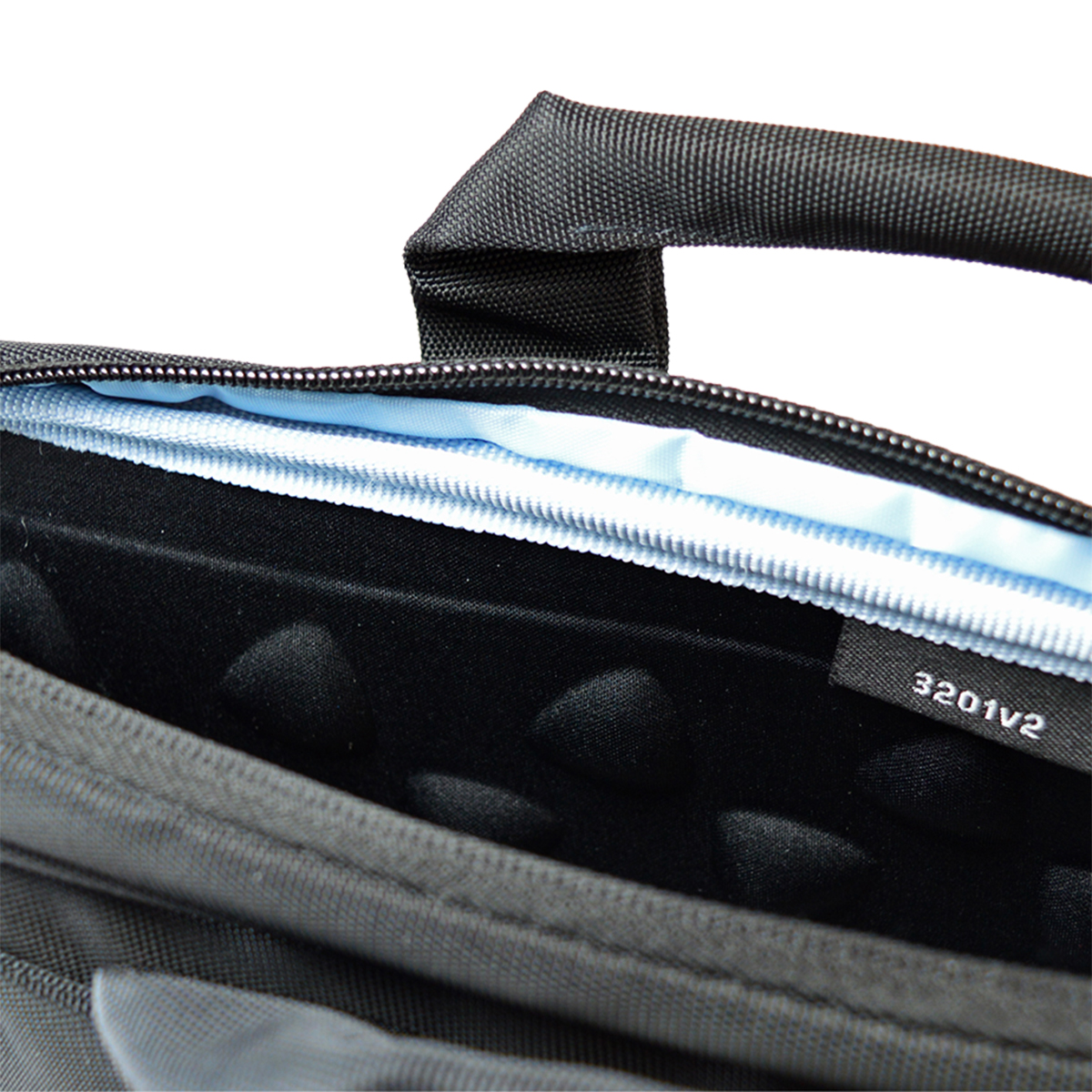 Nahaufnahme einer schwarzen Laptoptasche. Oben befindet sich ein Griff. Die Tasche hat einen Reißverschluss und ein hellblaues Innenfutter. Ein Etikett lautet '3201v2'.