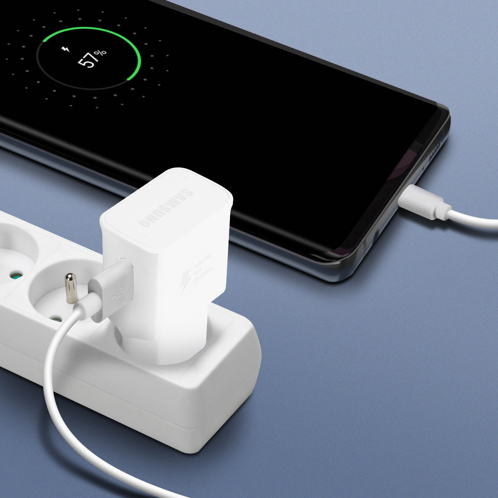 Un téléphone se chargeant à 57% avec un chargeur blanc branché sur une multiprise. Fond bleu.