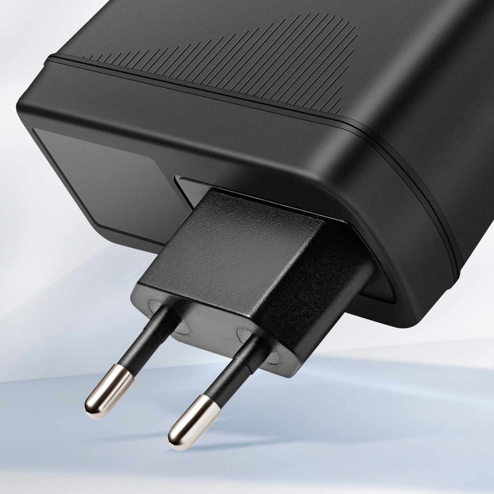 Czarny zasilacz ze srebrnymi końcówkami skierowany jest w stronę widza, na tle gradientu.