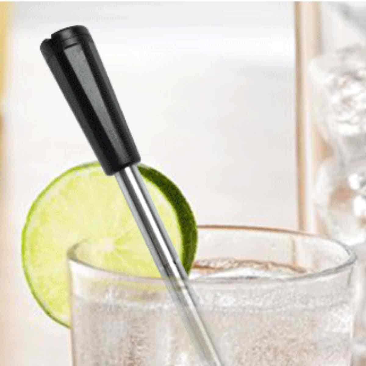 Ein Getränk wird mit einem langen Strohhalm umgerührt. Eine Limettenscheibe befindet sich im Glas. Der Rührer hat einen schwarzen Griff.