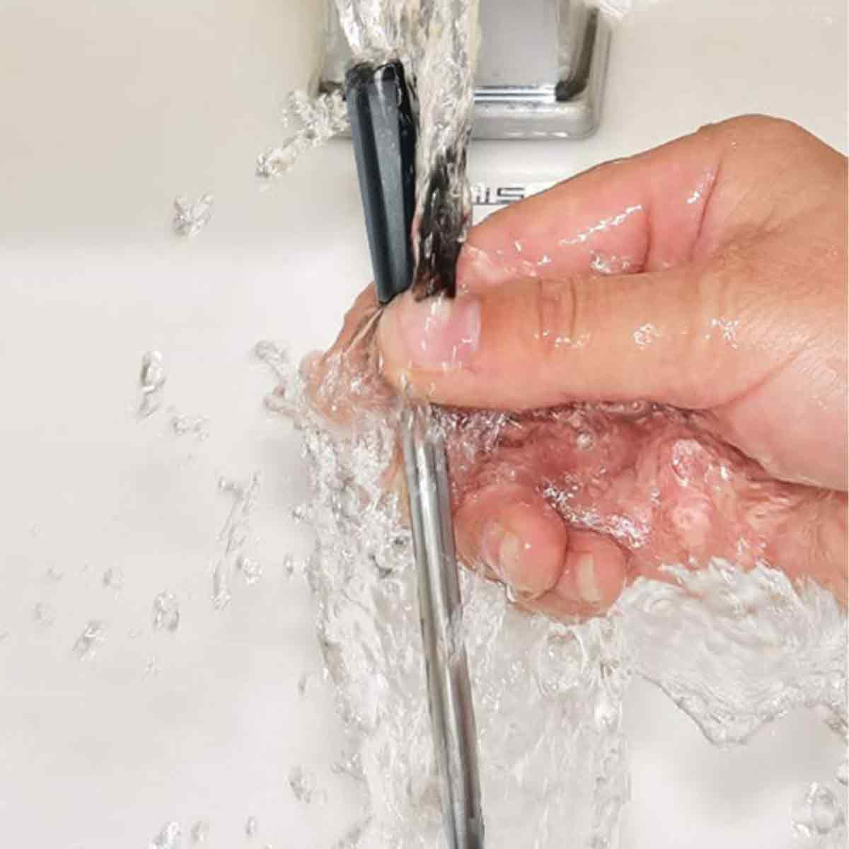 Eine Hand hält einen schwarzen Gegenstand unter fließendem Wasser. Das Wasser fließt über die Hand und den Gegenstand.