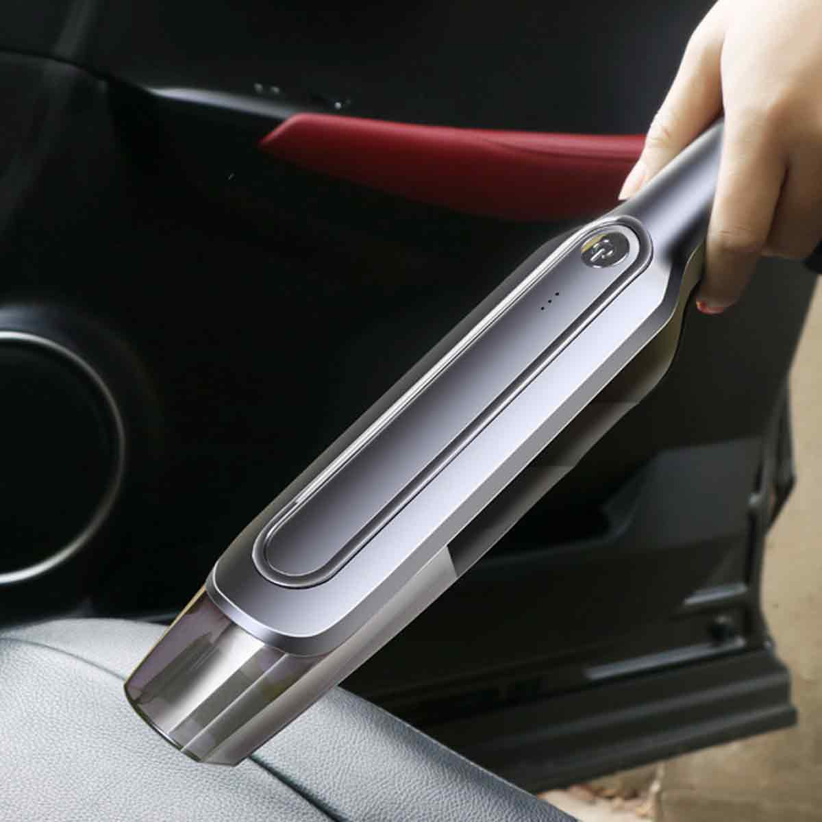 Eine Hand hält einen silber-schwarzen Autostaubsauger über einem Autositz. Die Tür und das rote Interieur sind im Hintergrund sichtbar.