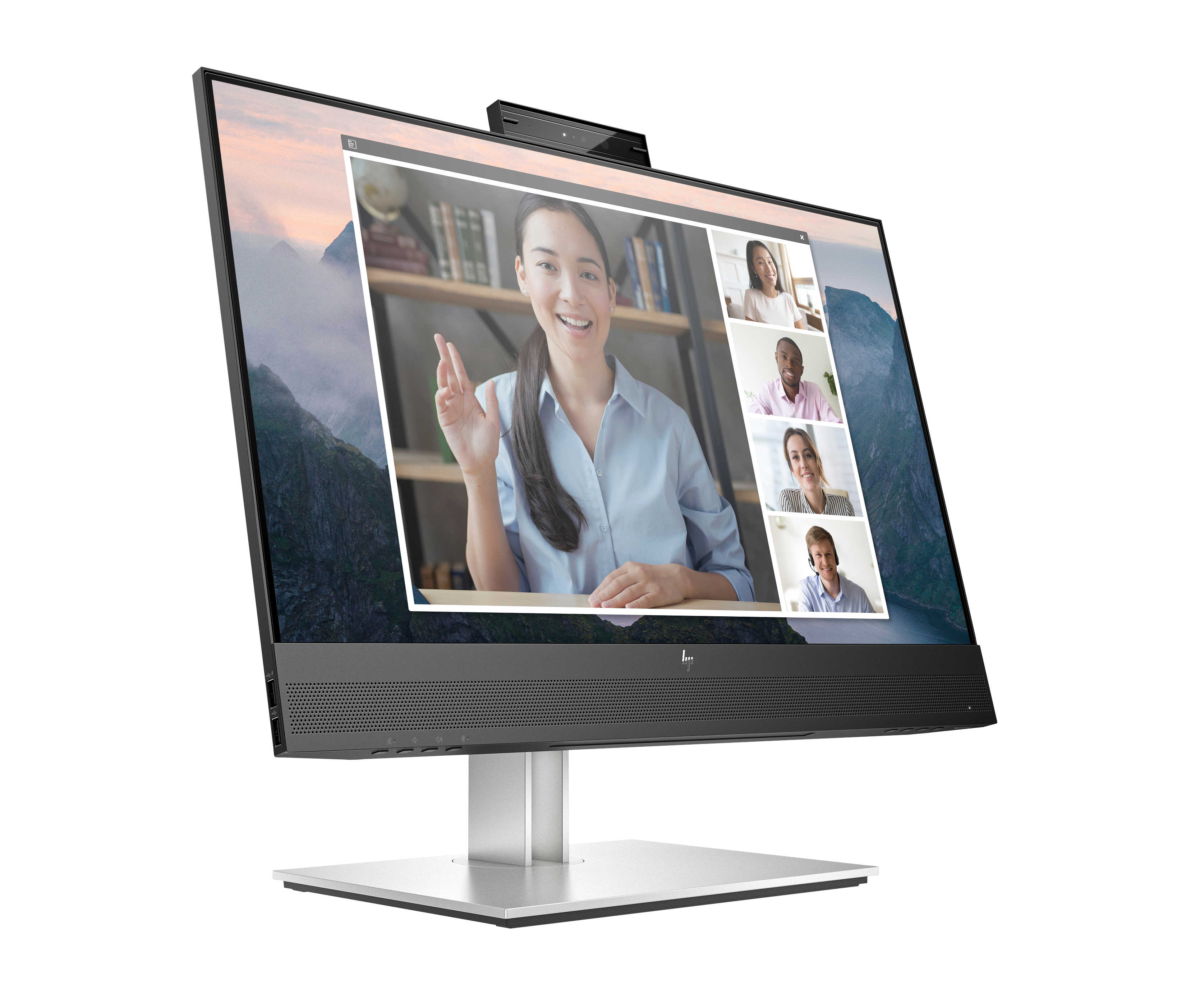 Una computadora todo en uno muestra una videollamada. Una mujer saluda en la ventana principal. Montañas al fondo.