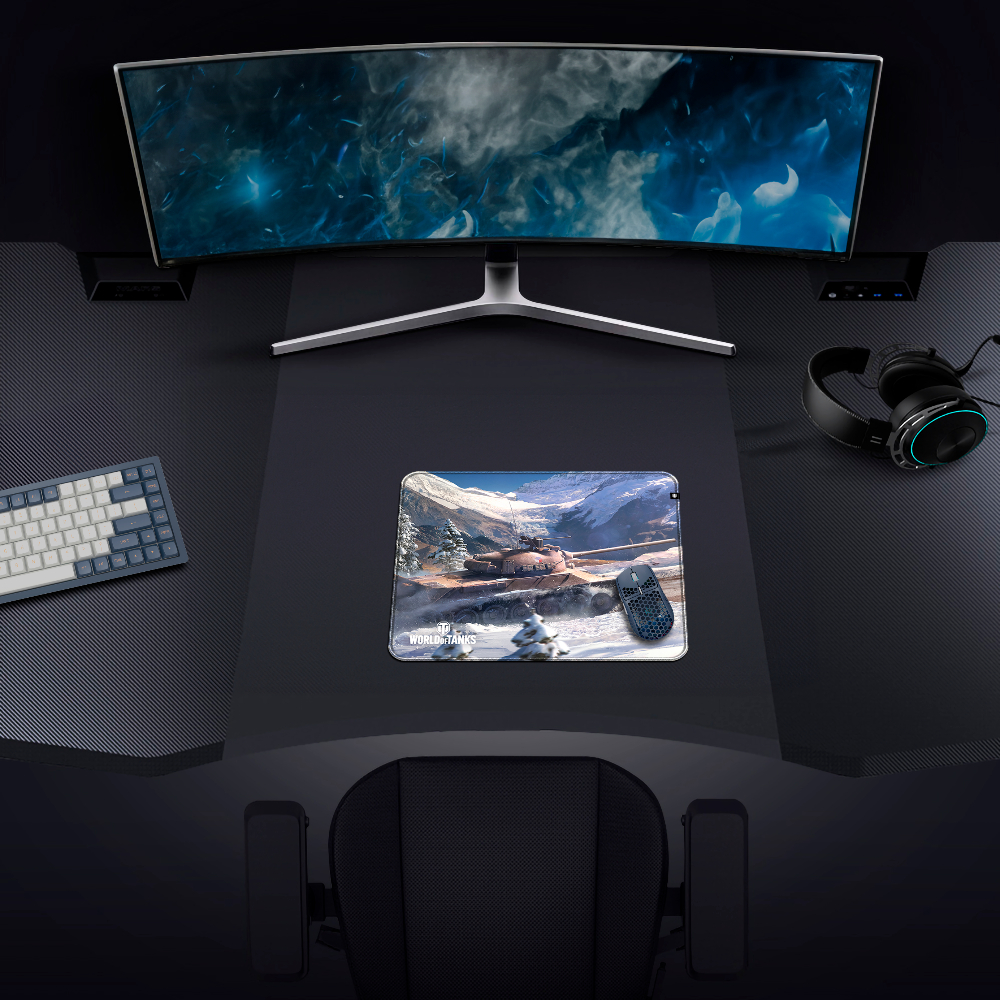 Configurazione di gioco: monitor curvo, tastiera, mouse, cuffie e tappetino con scena di carro armato. Scrivania e sedia nere.