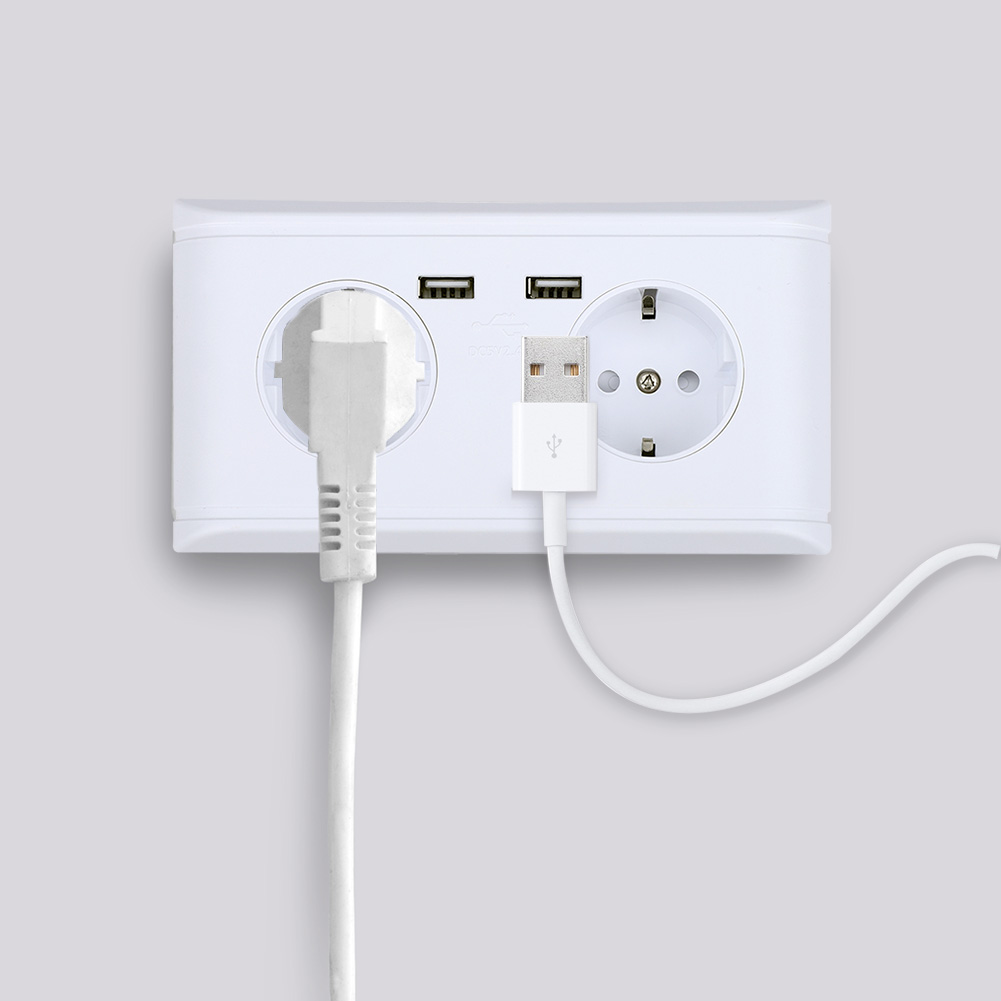 Eine weiße Steckdose mit zwei USB-Anschlüssen. Ein weißer Stecker steckt in der linken Steckdose. Ein USB-Kabel ist rechts eingesteckt.