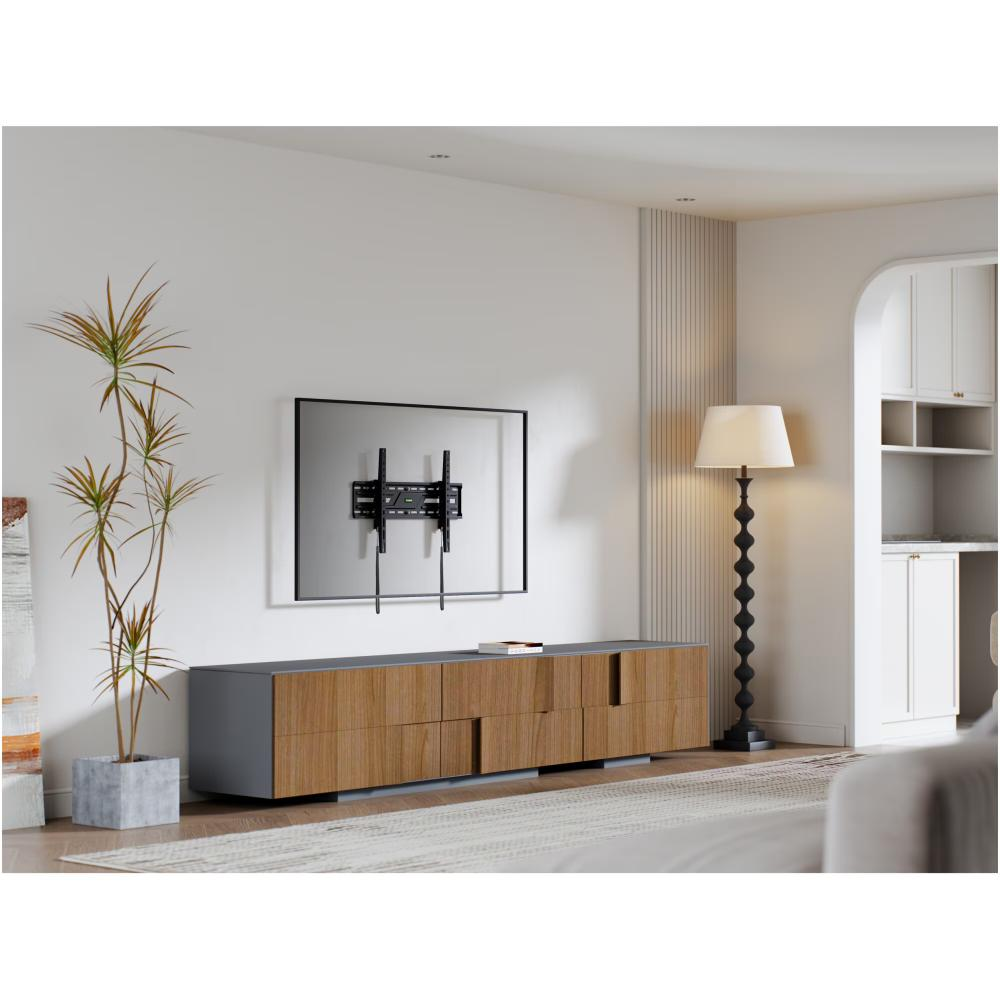 Moderne woonkamer met een tv aan de muur. Een houten kast eronder. Hoge plant, staande lamp en witte inbouwkasten.