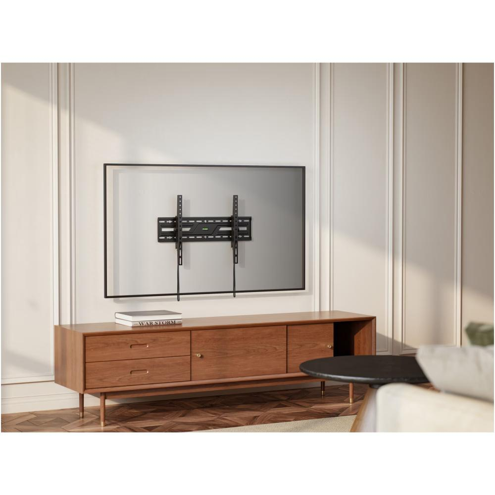 Een tv is gemonteerd op een witte muur. Onder de tv staat een houten kast. Een zwarte tafel en een bank staan ook in de kamer.