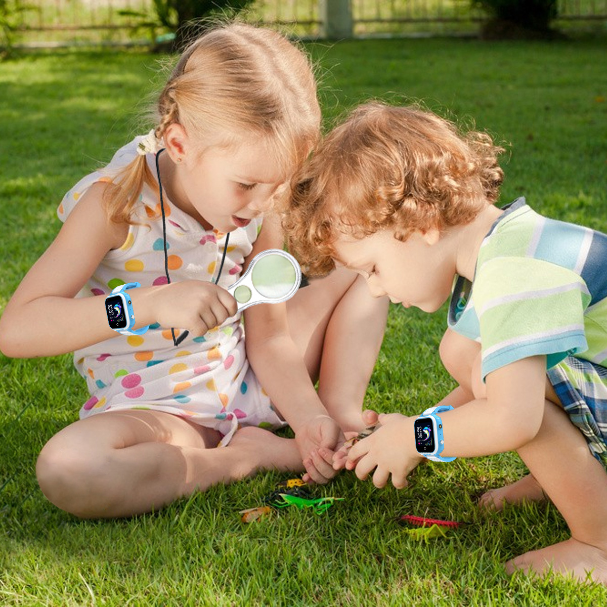 Zwei Kinder auf Gras untersuchen kleine Objekte. Eines hält eine Lupe. Beide tragen Smartwatches. Grünes Gras und blauer Himmel.