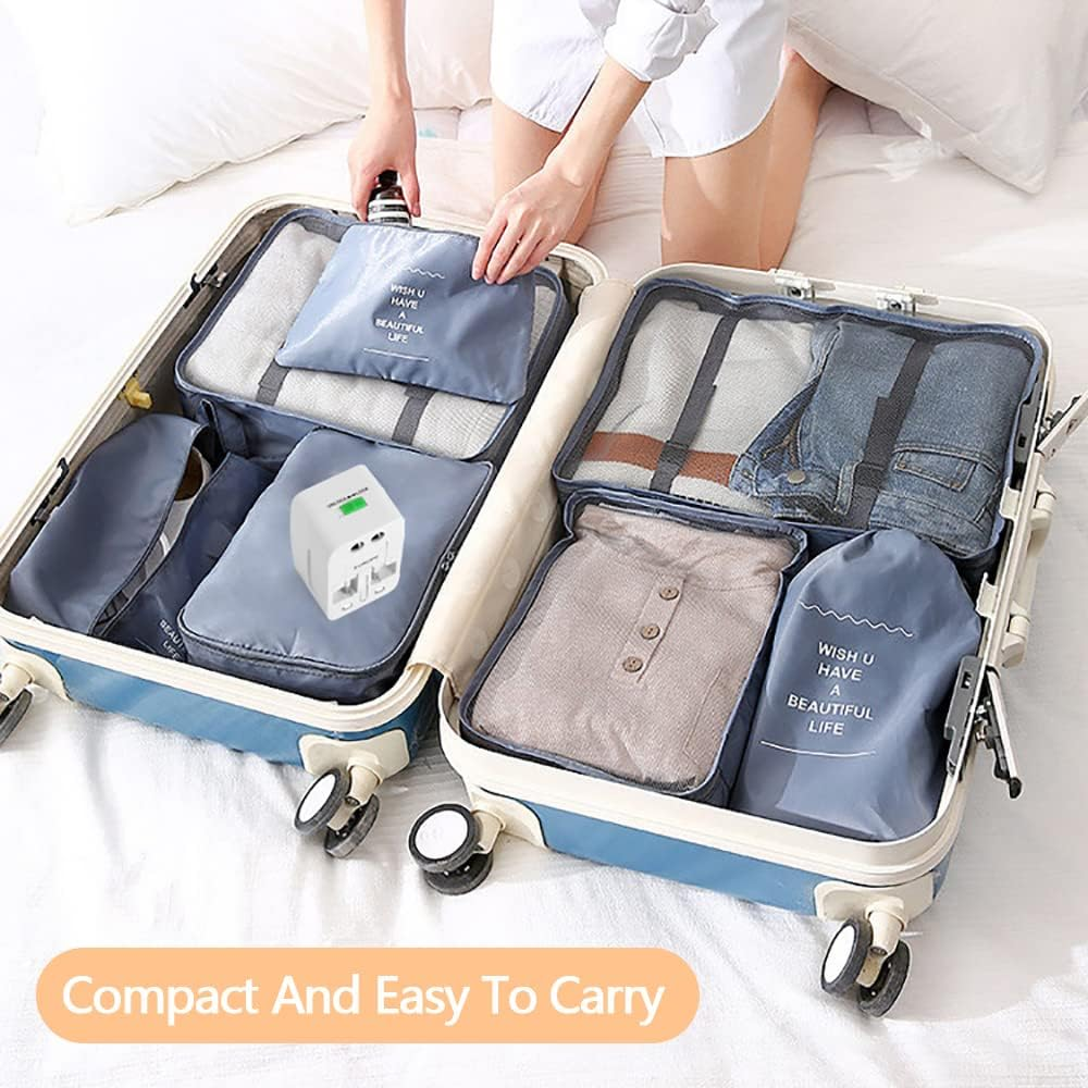 Offener Koffer mit Kleidung und Reisezubehör. Eine Person packt Kleidung in den Koffer. Der Koffer steht auf einem Bett.