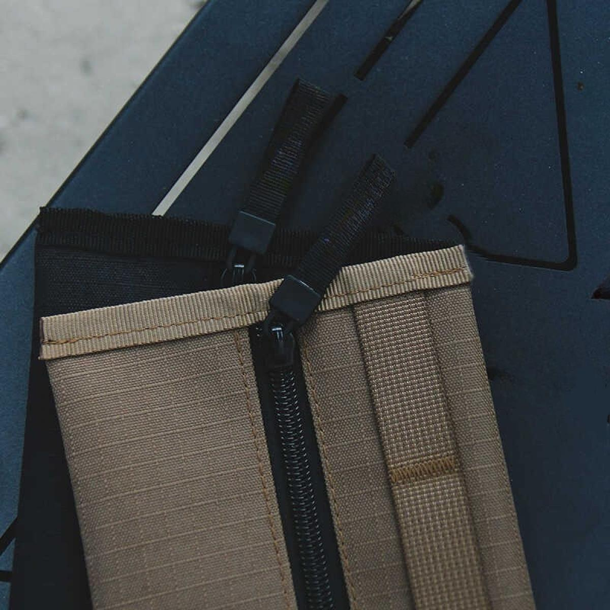 Zwei beige und schwarze Reißverschlusstaschen auf einer dunkelblauen Oberfläche. Reißverschlüsse und Zuglaschen sind schwarz. Textur auf den Taschen sichtbar.