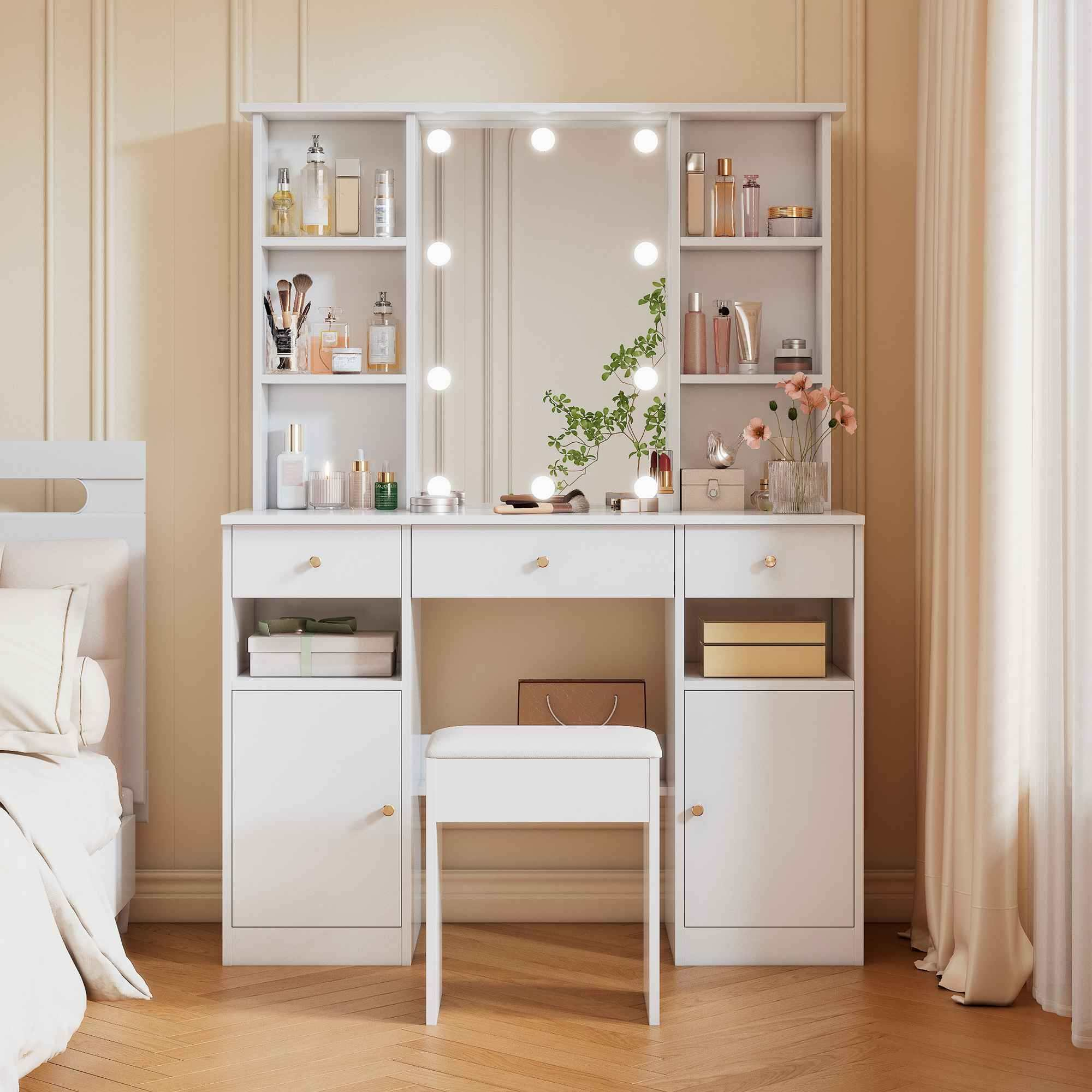 Ein weißer Schminktisch mit Spiegel und Lichtern, Kosmetika, einem Hocker und einem Holzboden. Auf der linken Seite befindet sich ein Bett.