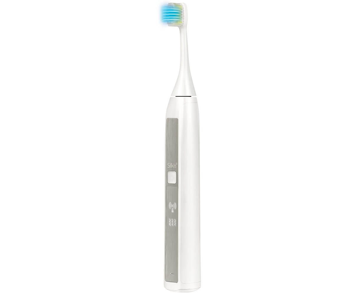 Une brosse à dents électrique blanche avec un panneau argenté. La tête de brosse brille en bleu/vert. La brosse est verticale, centrée sur fond blanc.