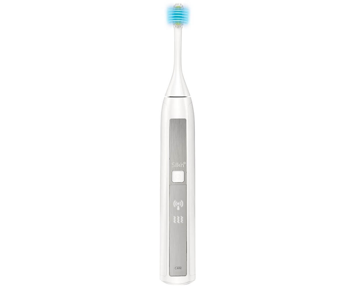 Brosse à dents électrique blanche avec des poils bleus. Elle possède un panneau argenté avec la marque Silkn et plusieurs voyants.