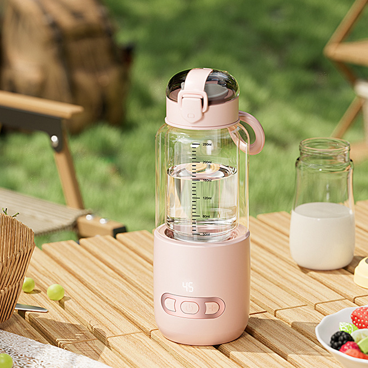 Eine rosa-transparente Wasserflasche mit Digitalanzeige, ein Glas Milch, Obst und Trauben auf einem Holztisch im Freien.