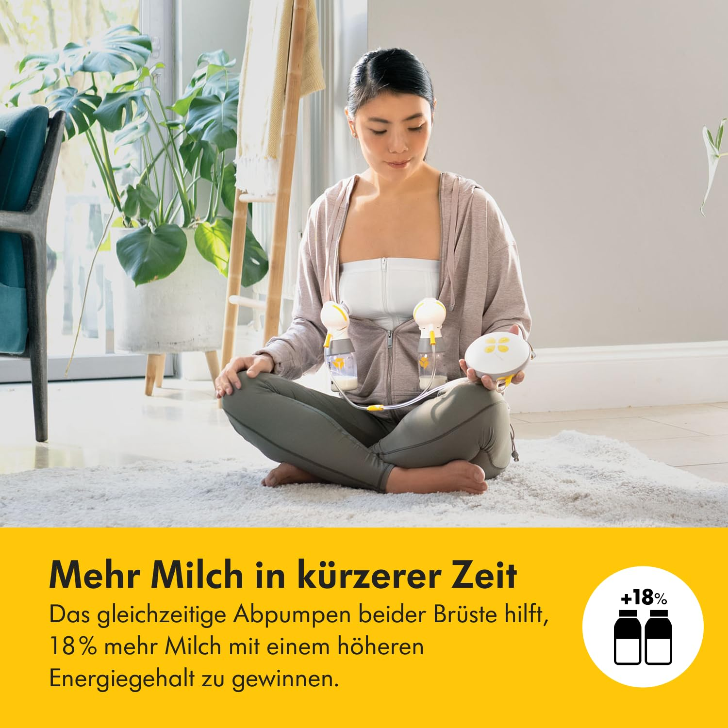 Frau benutzt eine Brustpumpe. Sie sitzt auf einem Teppich und hält die Pumpe, mit Pflanzen und einem Fenster im Hintergrund.