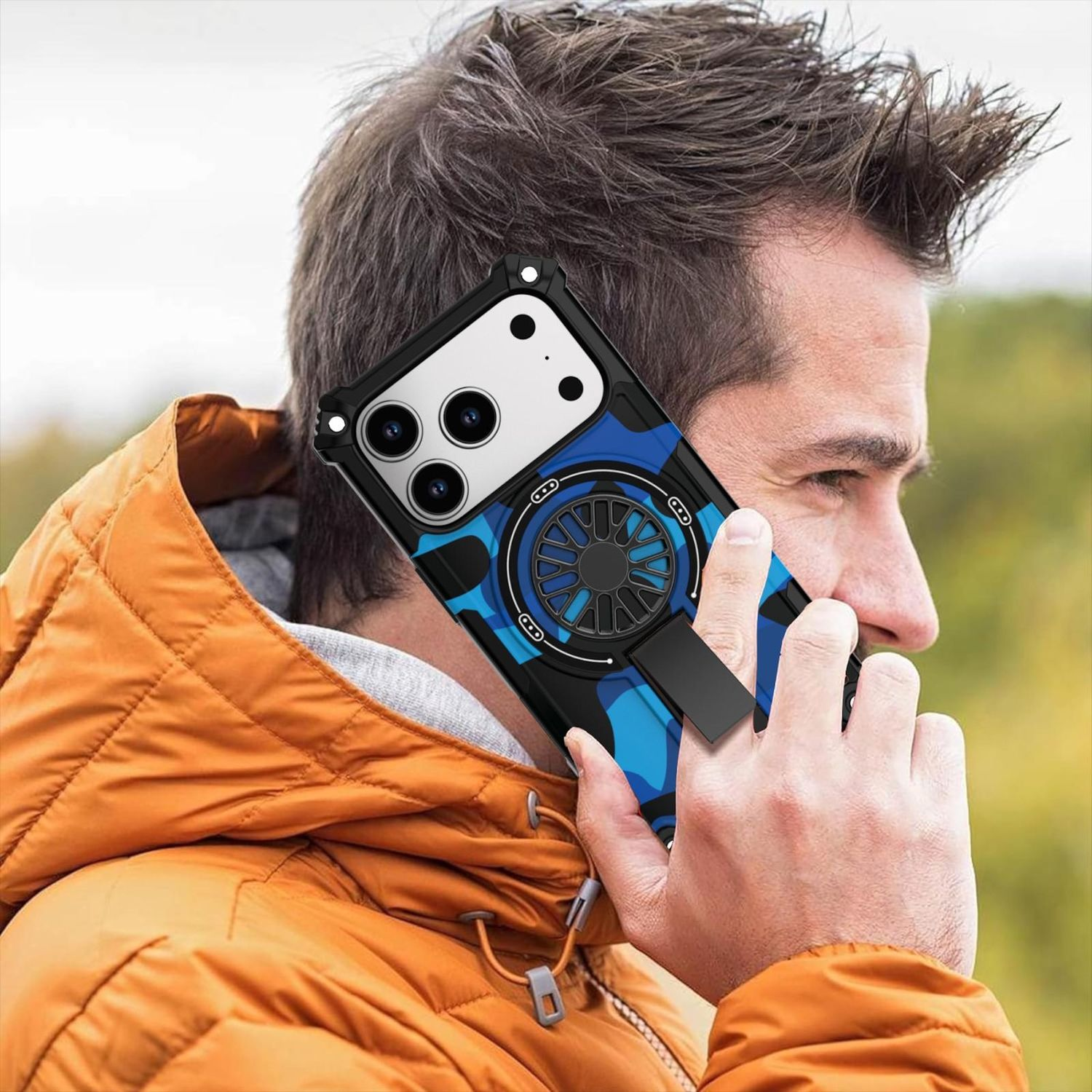 Ein Mann hält ein Telefon mit einer blauen Camouflage-Hülle an sein Ohr. Er trägt eine orange Jacke. Der Hintergrund ist verschwommen grün.