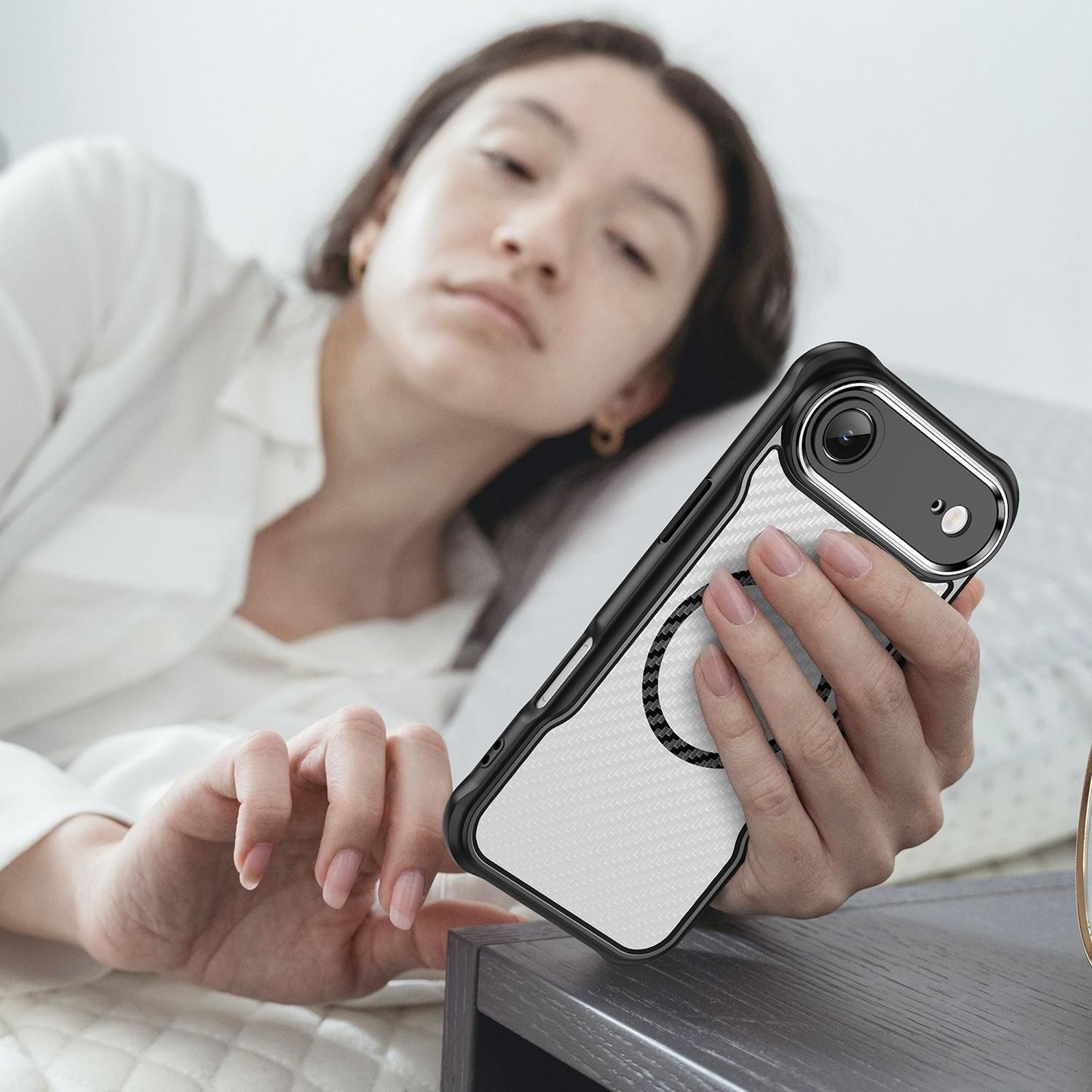 Eine Frau im Bett hält ein Telefon mit weißer und schwarzer Hülle. Sie stützt ihren Kopf auf ein Kissen, das Telefon ist im Fokus.