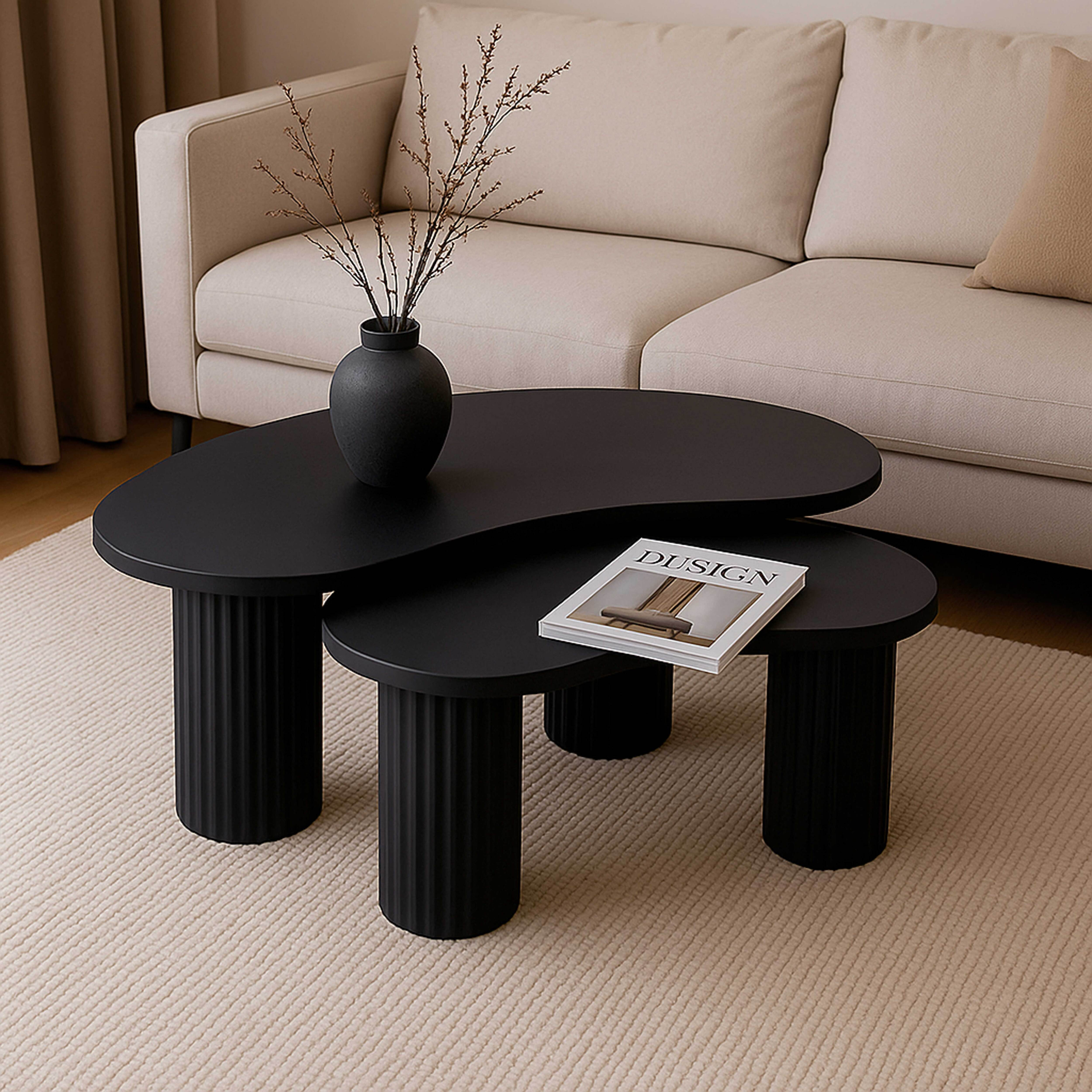 Schwarze Couchtische mit einer Zeitschrift und einer Vase mit Zweigen vor einem beigen Sofa auf einem Teppich.
