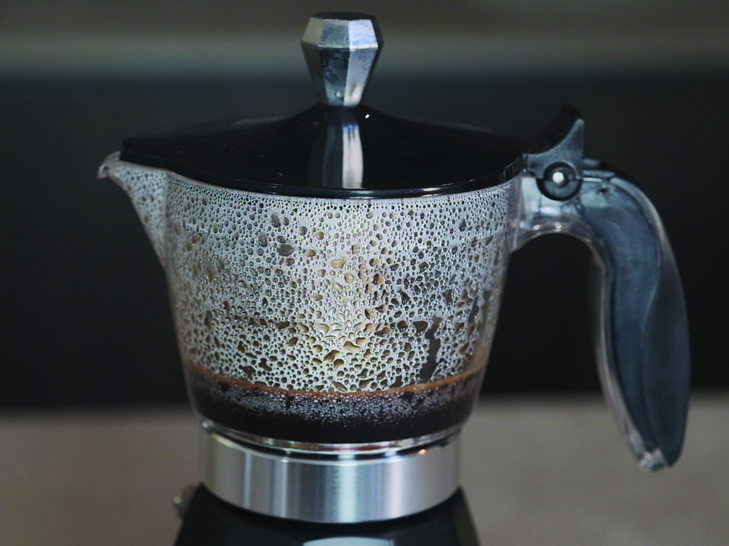 Una caffettiera con un serbatoio di vetro pieno di caffè. Il coperchio e il manico sono neri.