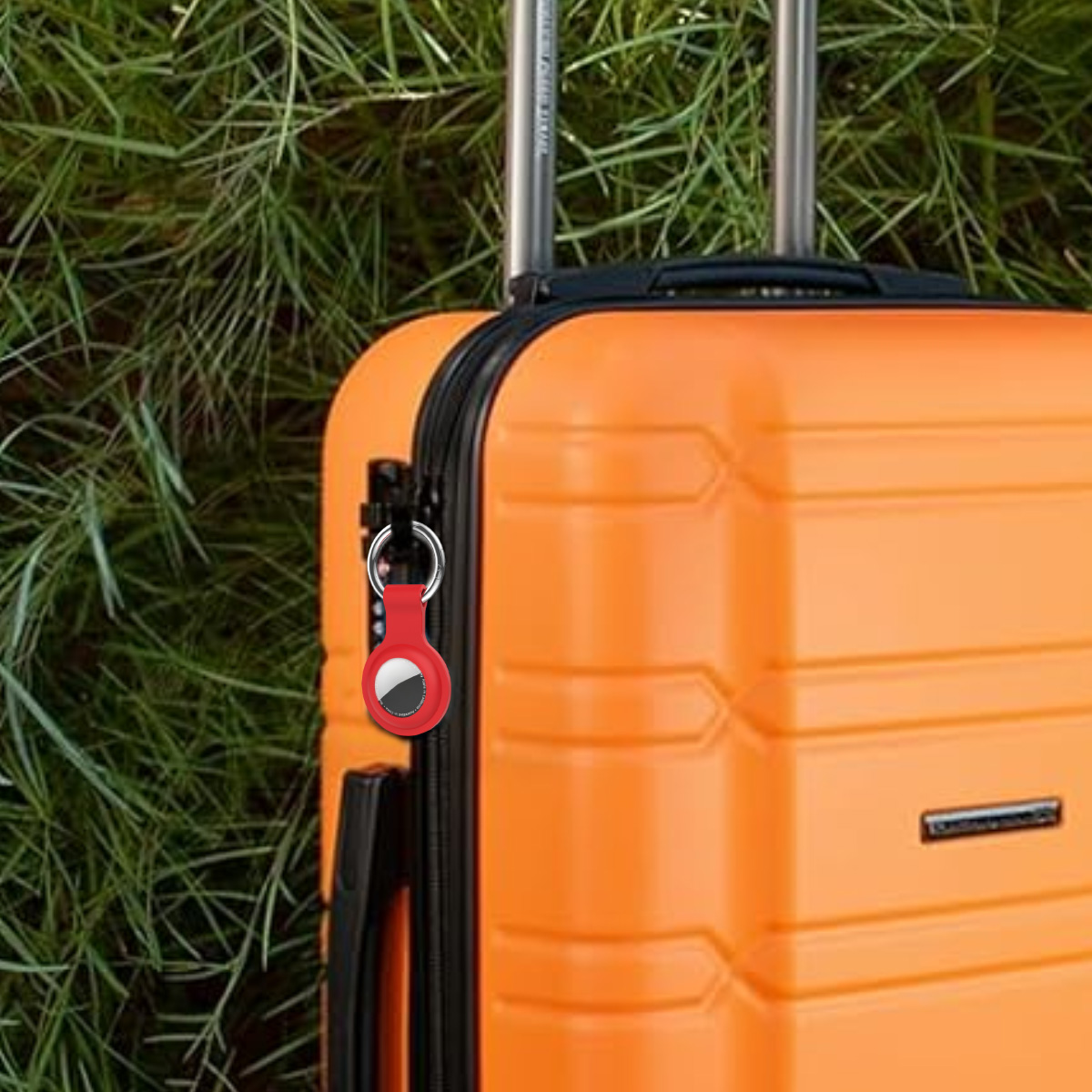 Ein orangefarbener Koffer mit einem roten Tracker. Der Hintergrund ist grünes Gras. Der Koffer hat silberne Griffe.