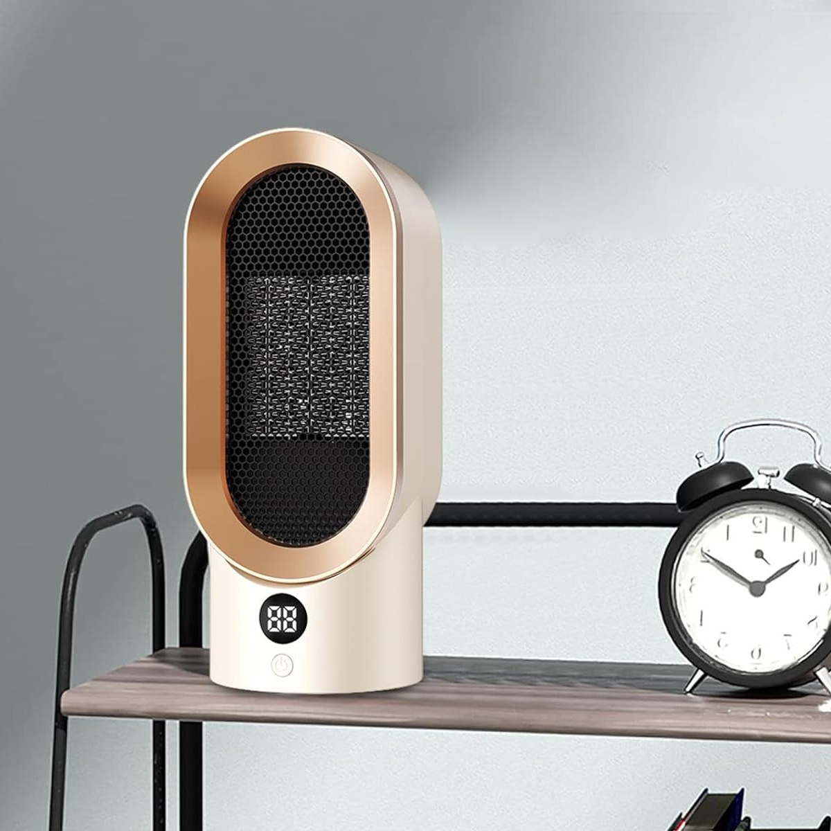 Ein beige-goldener Elektroheizer mit Digitalanzeige steht auf einem Regal neben einem schwarzen Wecker.