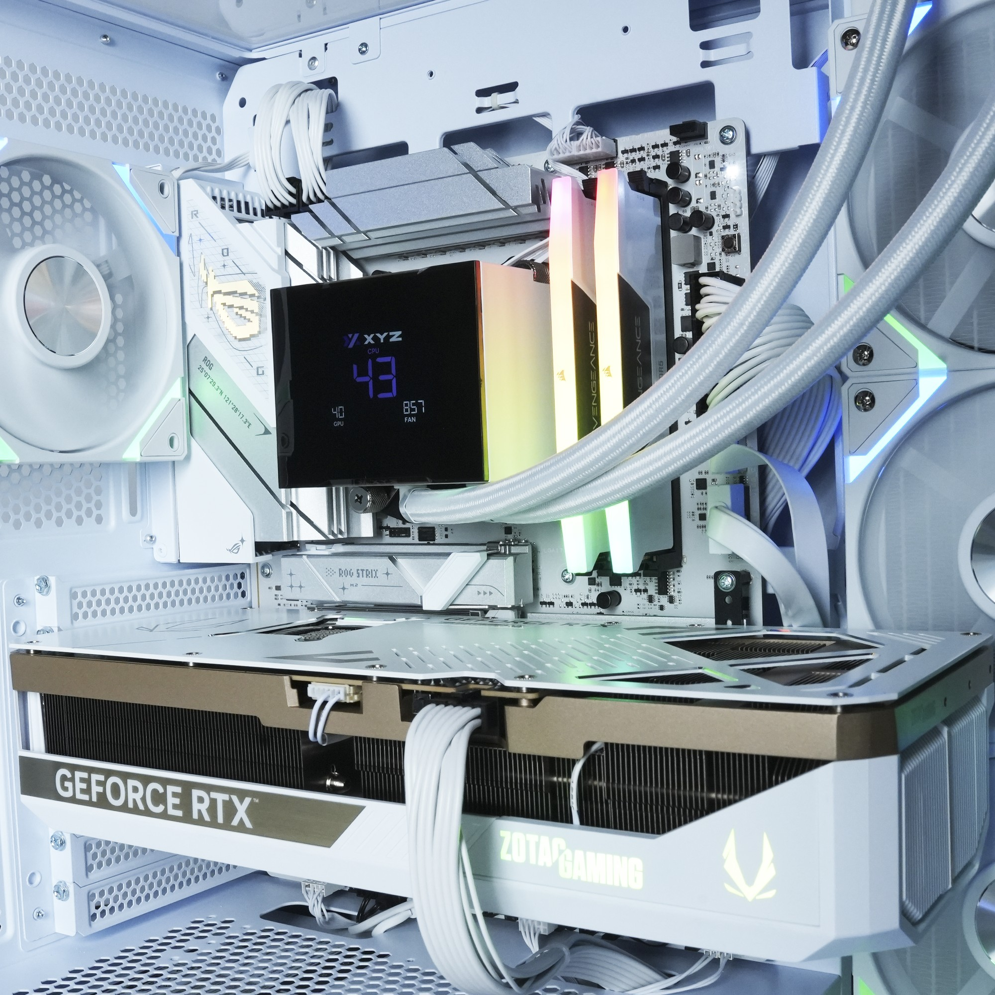 Interior de una caja de ordenador con tarjeta gráfica, refrigerador de CPU y RAM. Cables y ventiladores blancos. Pantalla muestra estadísticas.