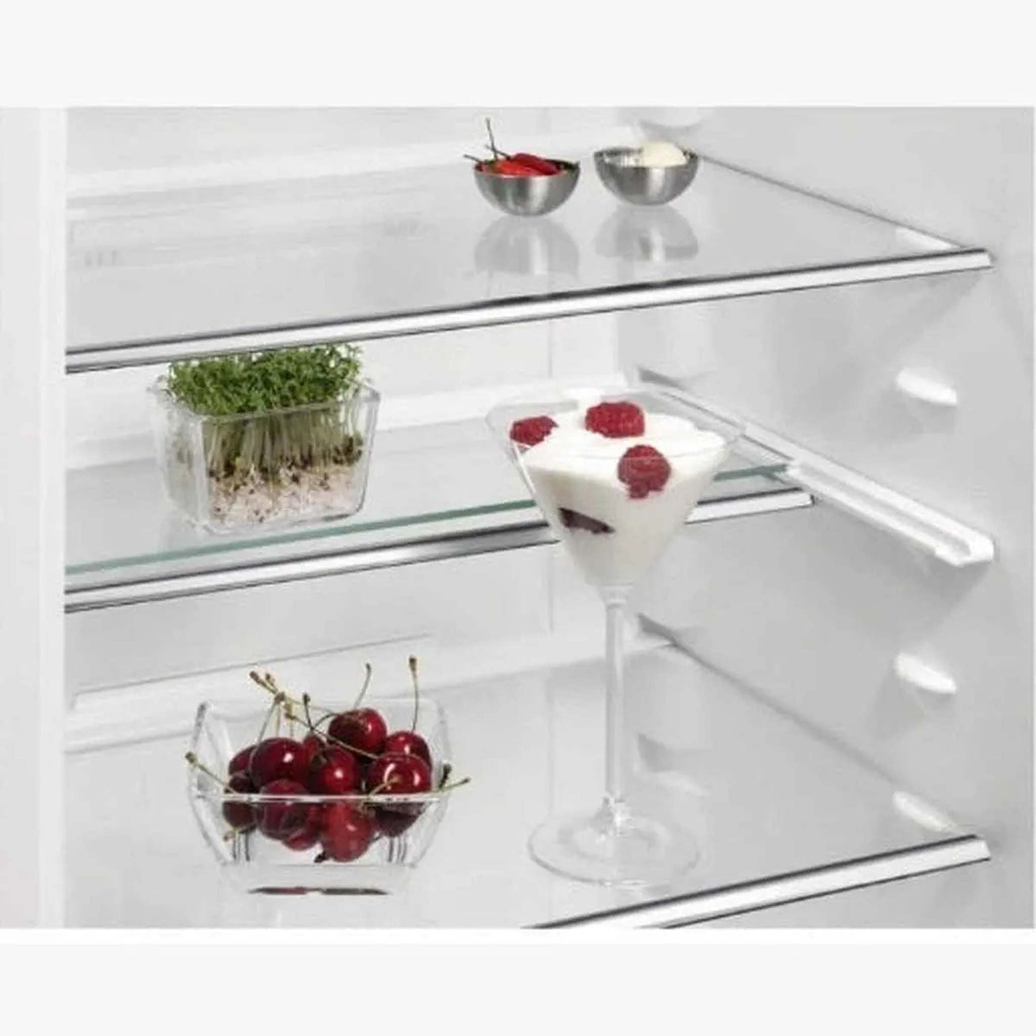 Koelkastinterieur met kruiden, kersen en dessert met frambozen. Glazen planken zichtbaar.