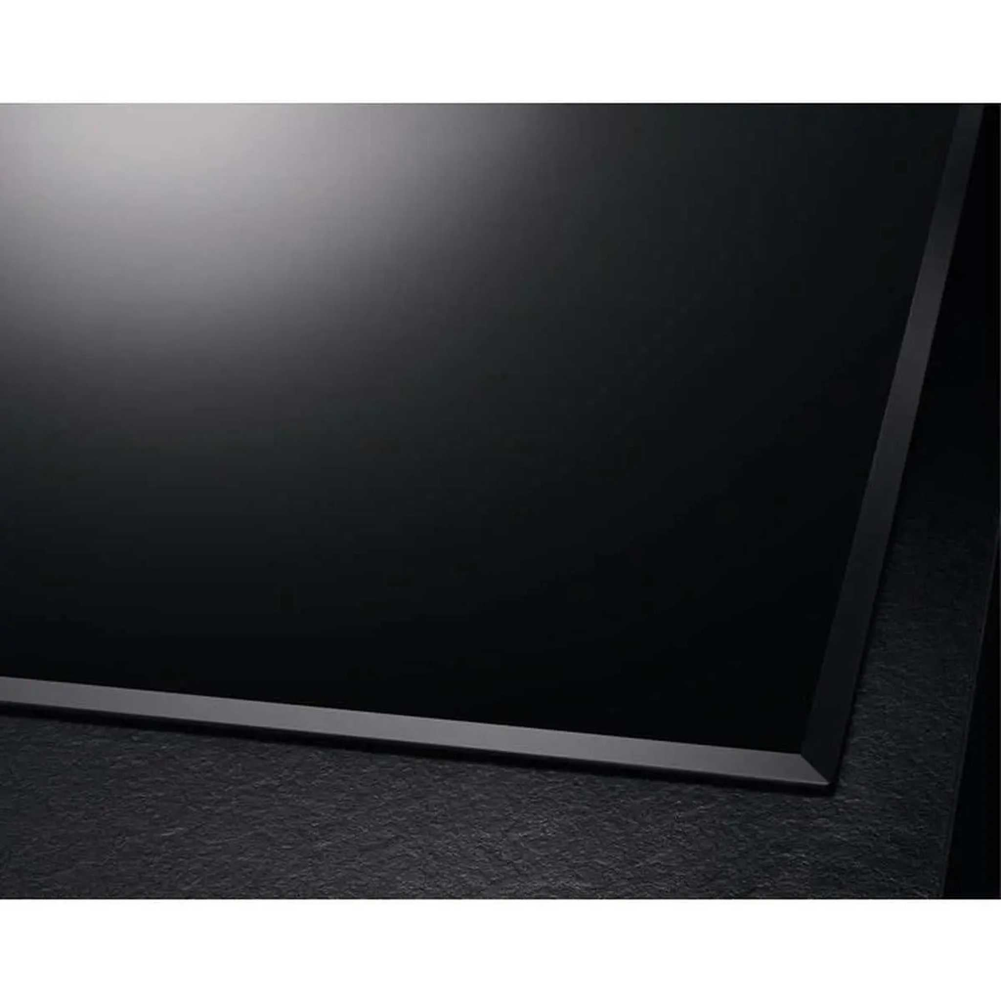 Primo piano di un piano cottura elettrico nero su una superficie nera strutturata. Piano cottura lucido e riflettente.