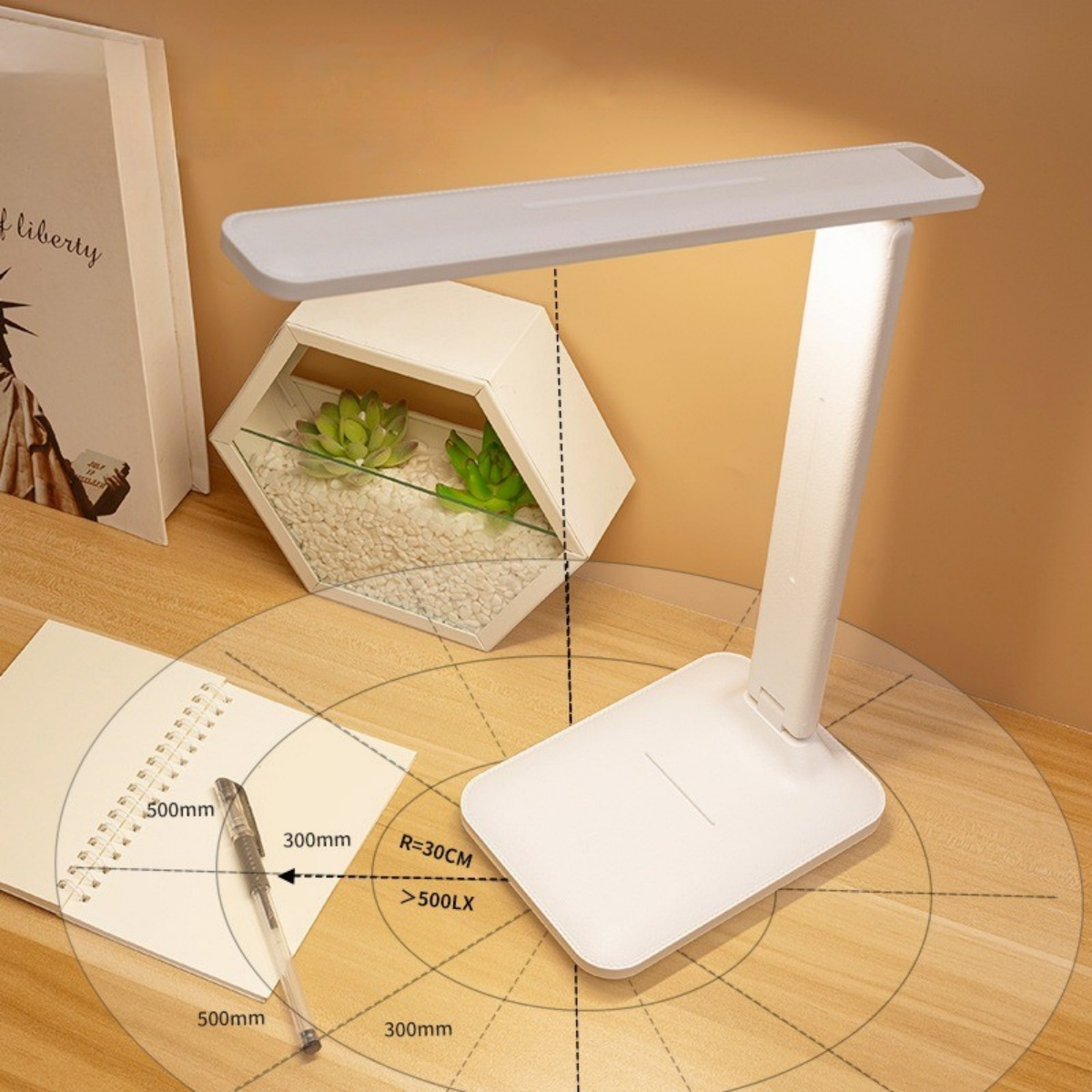 Eine weiße Schreibtischlampe beleuchtet einen Schreibtisch mit Notizbuch, Stift und einem dekorativen Terrarium mit Sukkulenten. Der Hintergrund ist beige.