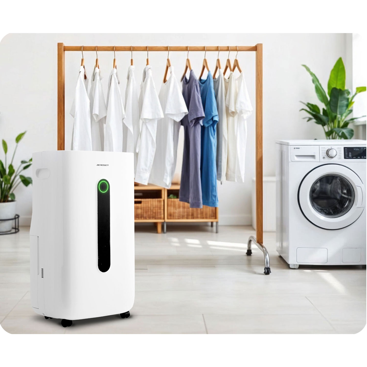 Biały osuszacz powietrza stoi obok drewnianego wieszaka na ubrania z koszulami. Po prawej stronie znajduje się pralka. Obecne są rośliny w doniczkach.