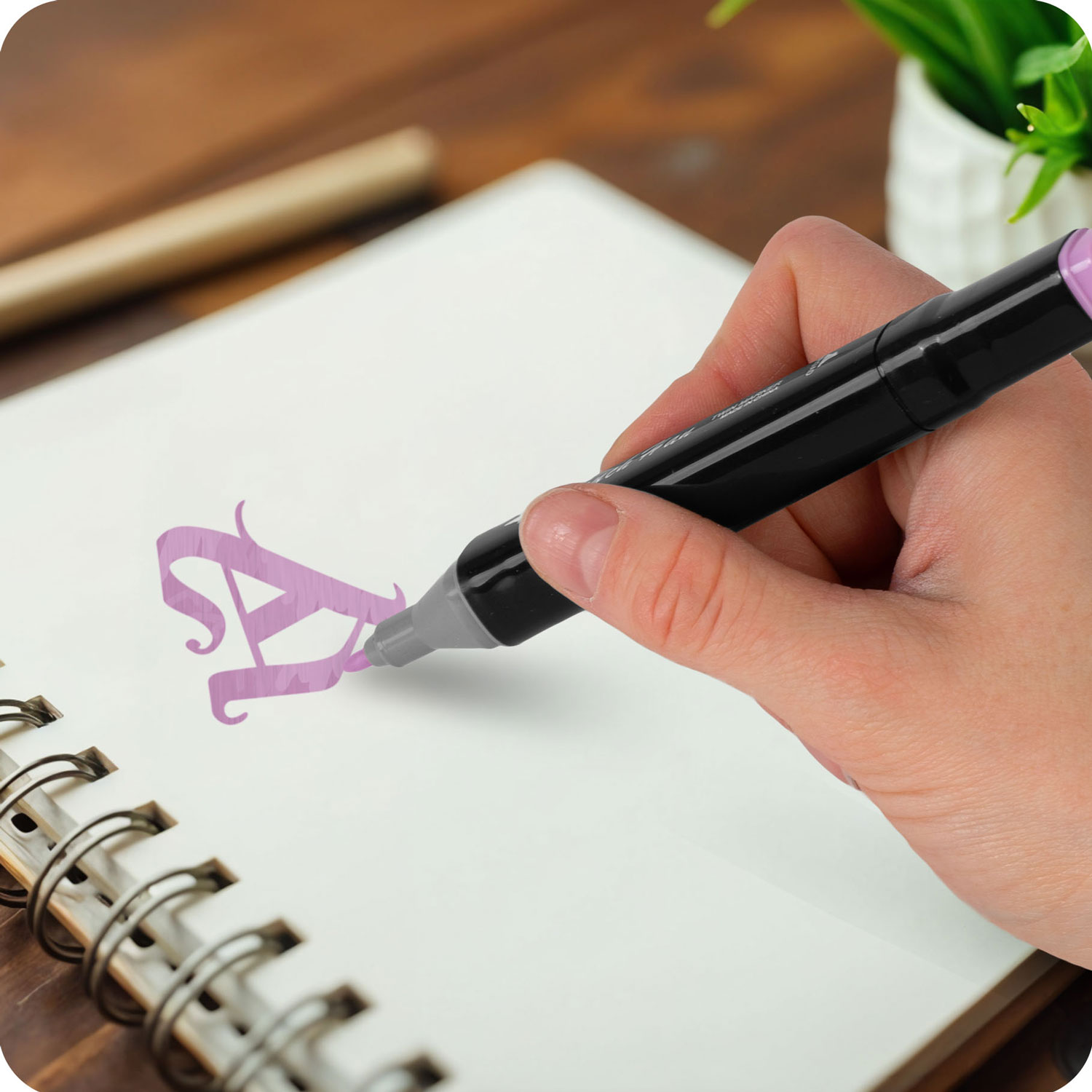 Ręka trzymająca czarny marker pisze w białym notatniku. Fioletowa litera „A” znajduje się na stronie.