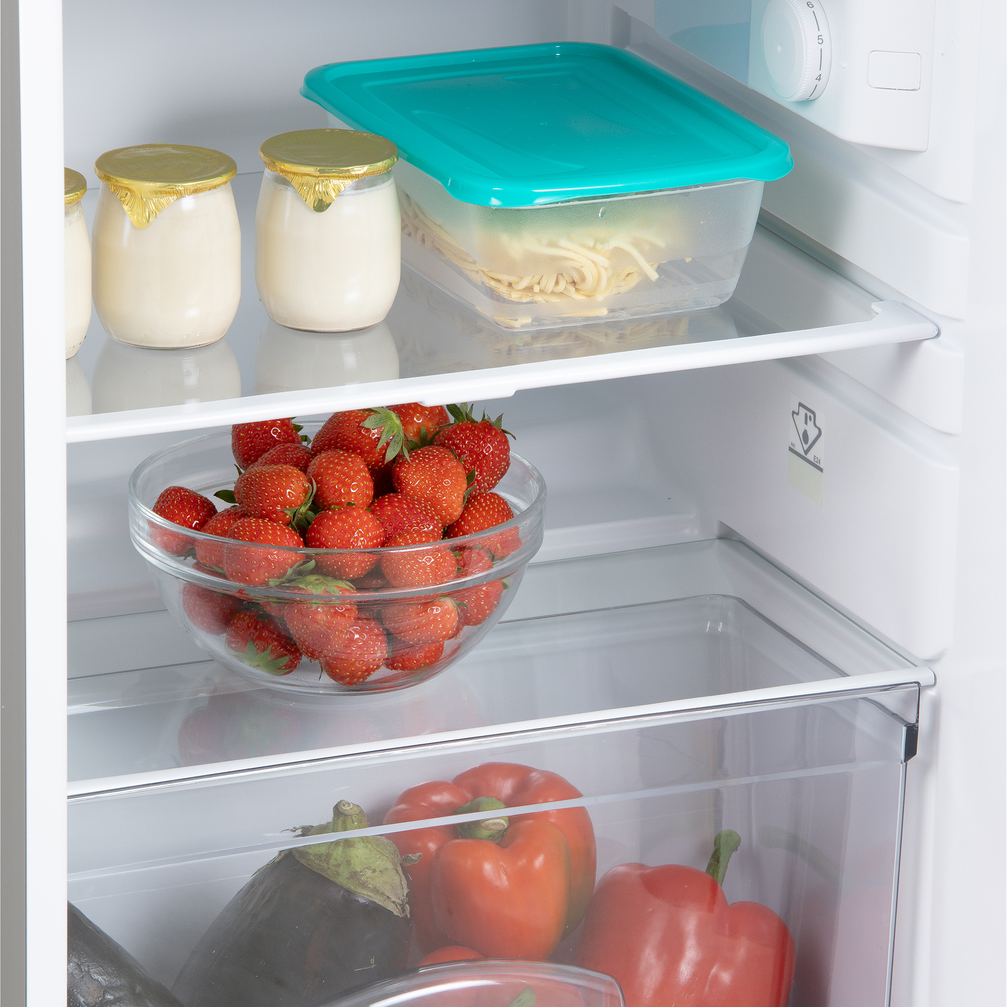 Dans un réfrigérateur: fraises dans un bol, yaourt, pâtes, poivrons et une aubergine.