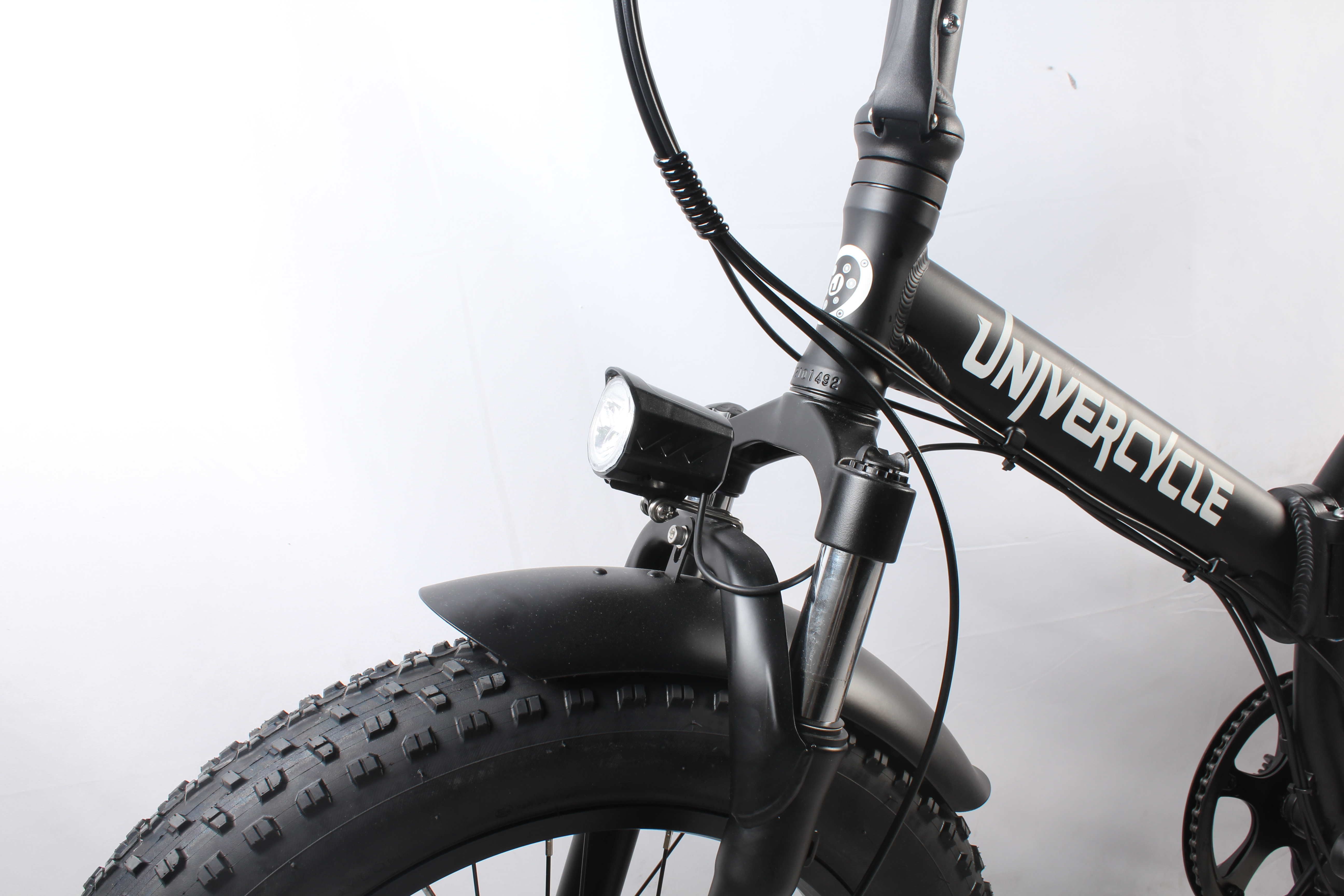 Primo piano di una bicicletta Univercycle nera. Mostra ruota anteriore, parafango, luce e manubrio. Sfondo bianco.