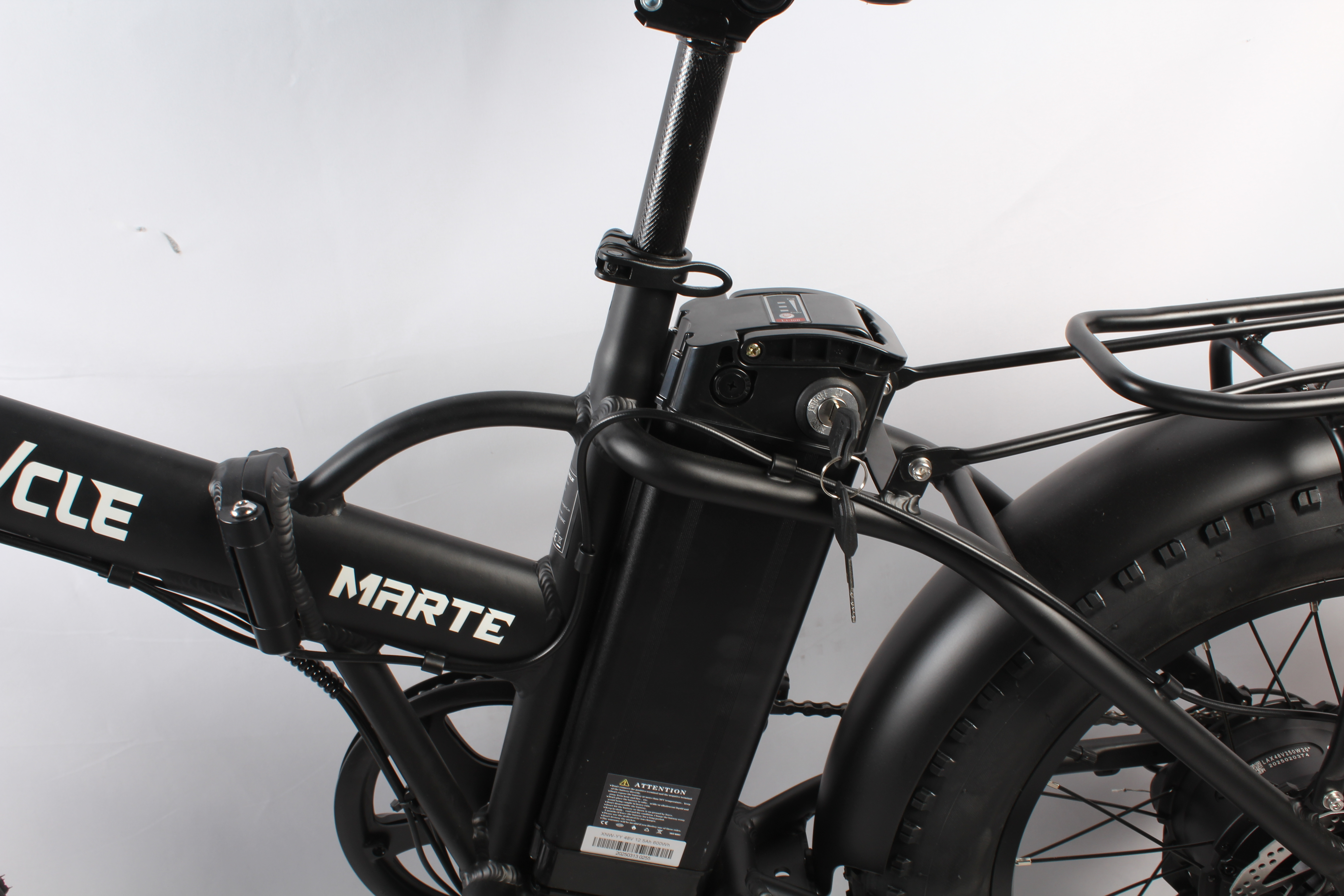 Bicicletta elettrica nera, MARTE sul telaio, batteria, chiavi nel quadro, pneumatici neri e portapacchi posteriore.