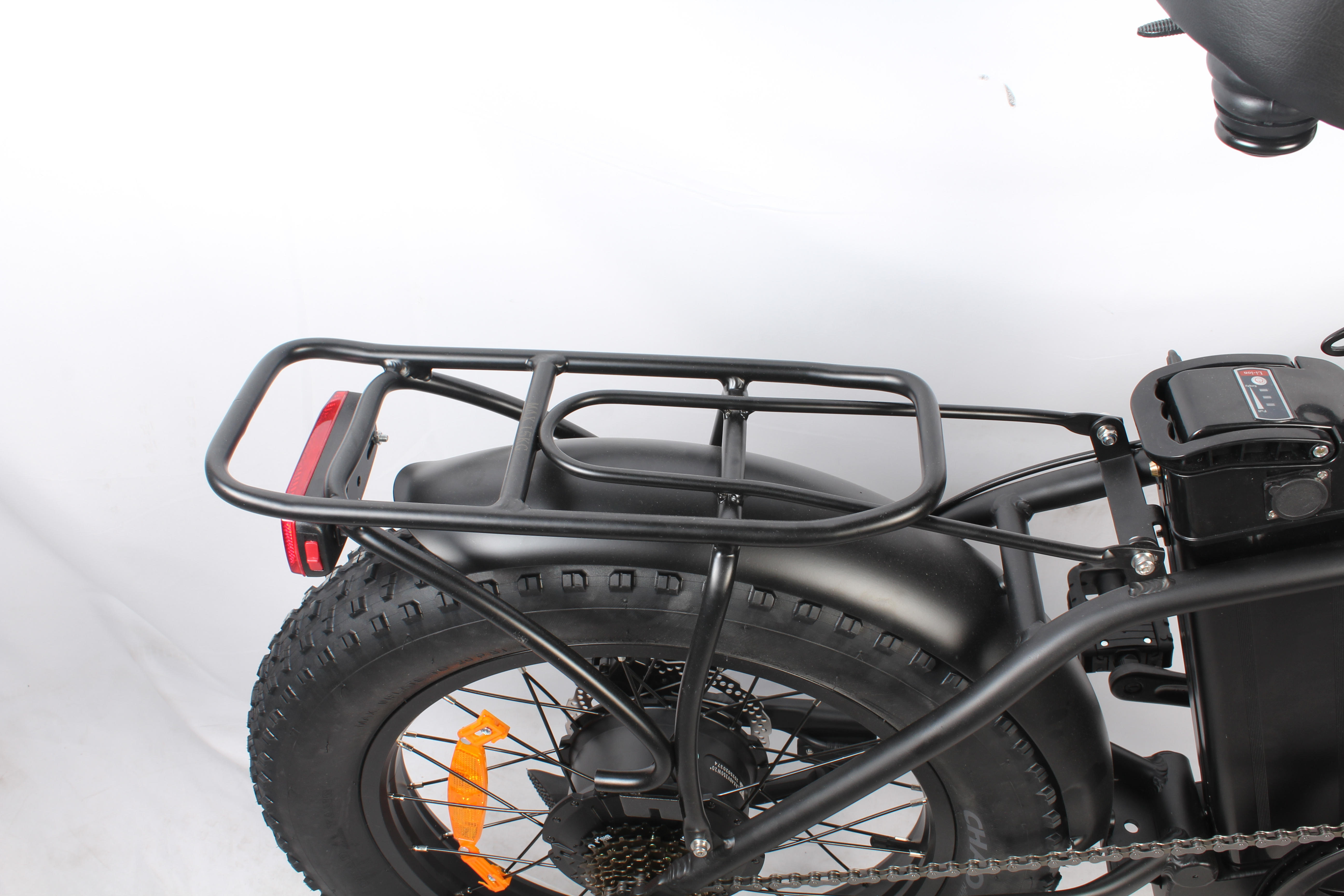 Primo piano della sezione posteriore di una e-bike. Telaio, pneumatico, portapacchi e fanale neri. Lo sfondo è bianco.