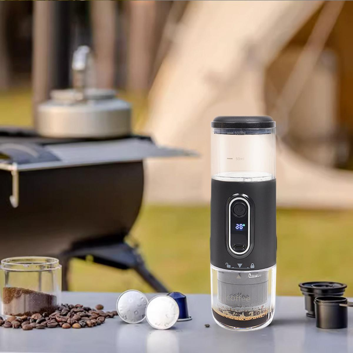 Tragbarer Kaffeezubereiter auf einem Tisch mit Kaffeebohnen und Kapseln. Ein Campingkocher ist im Hintergrund. Der Bereiter hat ein Digitaldisplay.