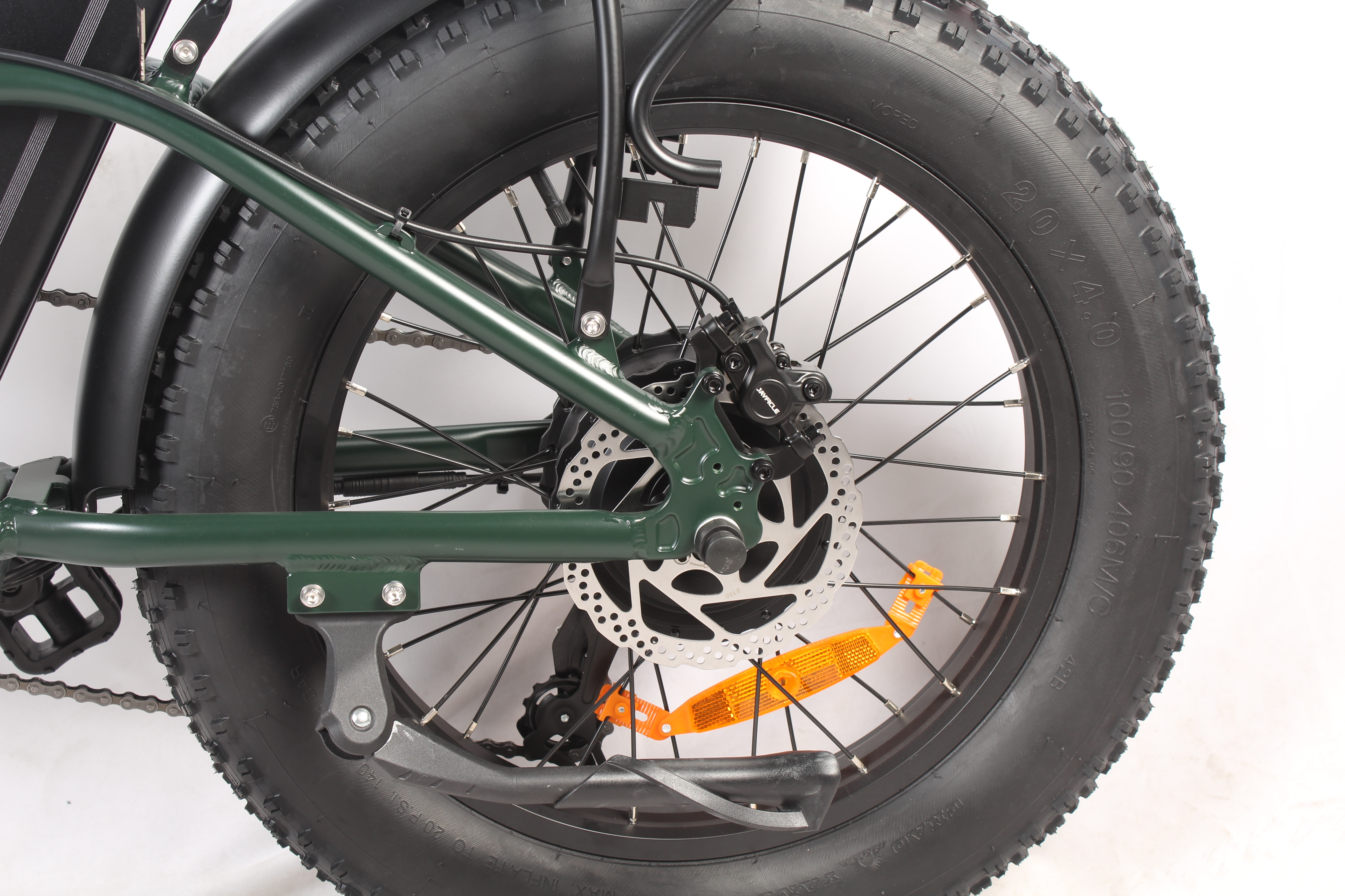 Primo piano di una ruota di bicicletta. Il pneumatico è nero e spesso. Un freno a disco è visibile con un catarifrangente arancione.