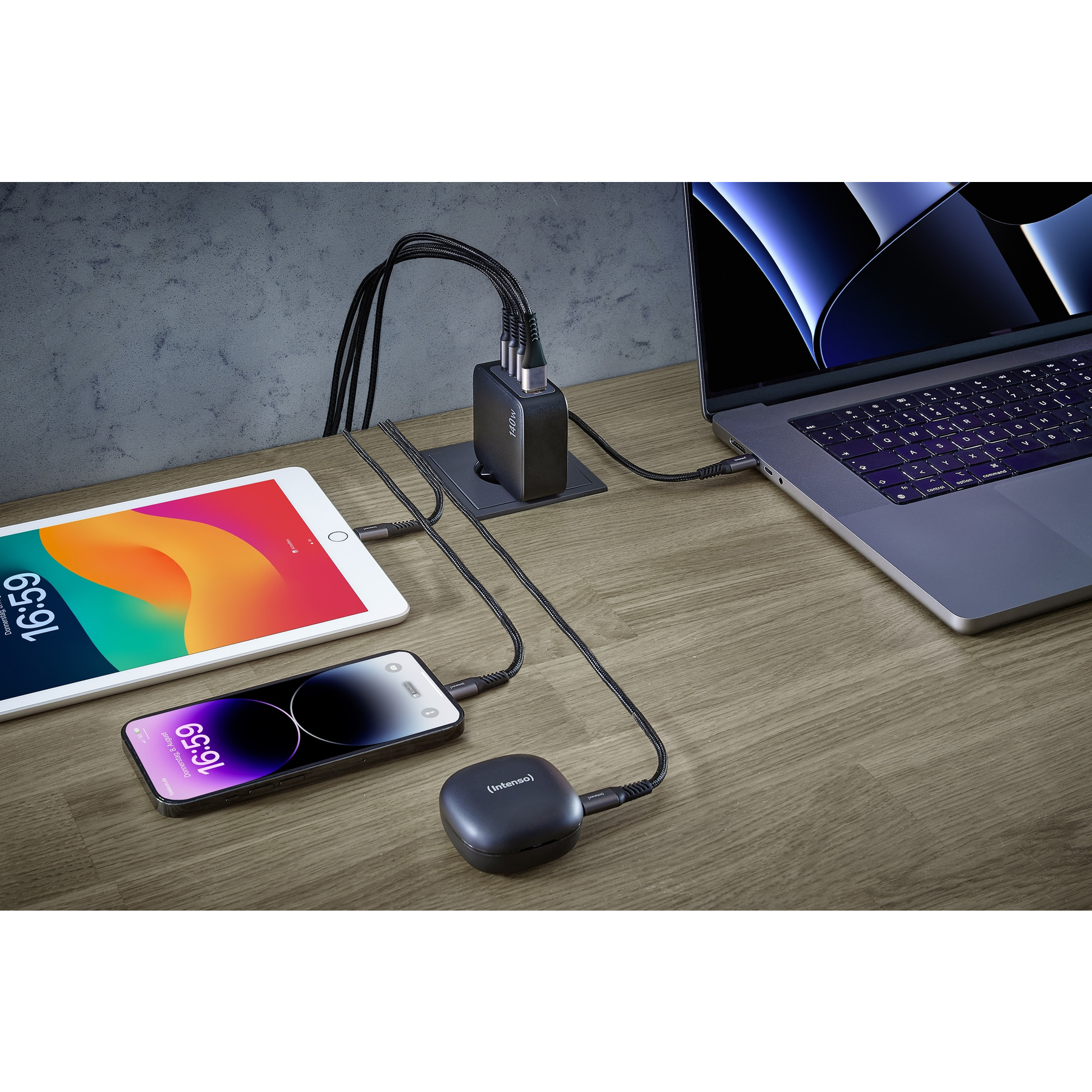 A desk with a laptop, tablet, and phone, all charging via a multi-port charger. Time displayed is 16:59.