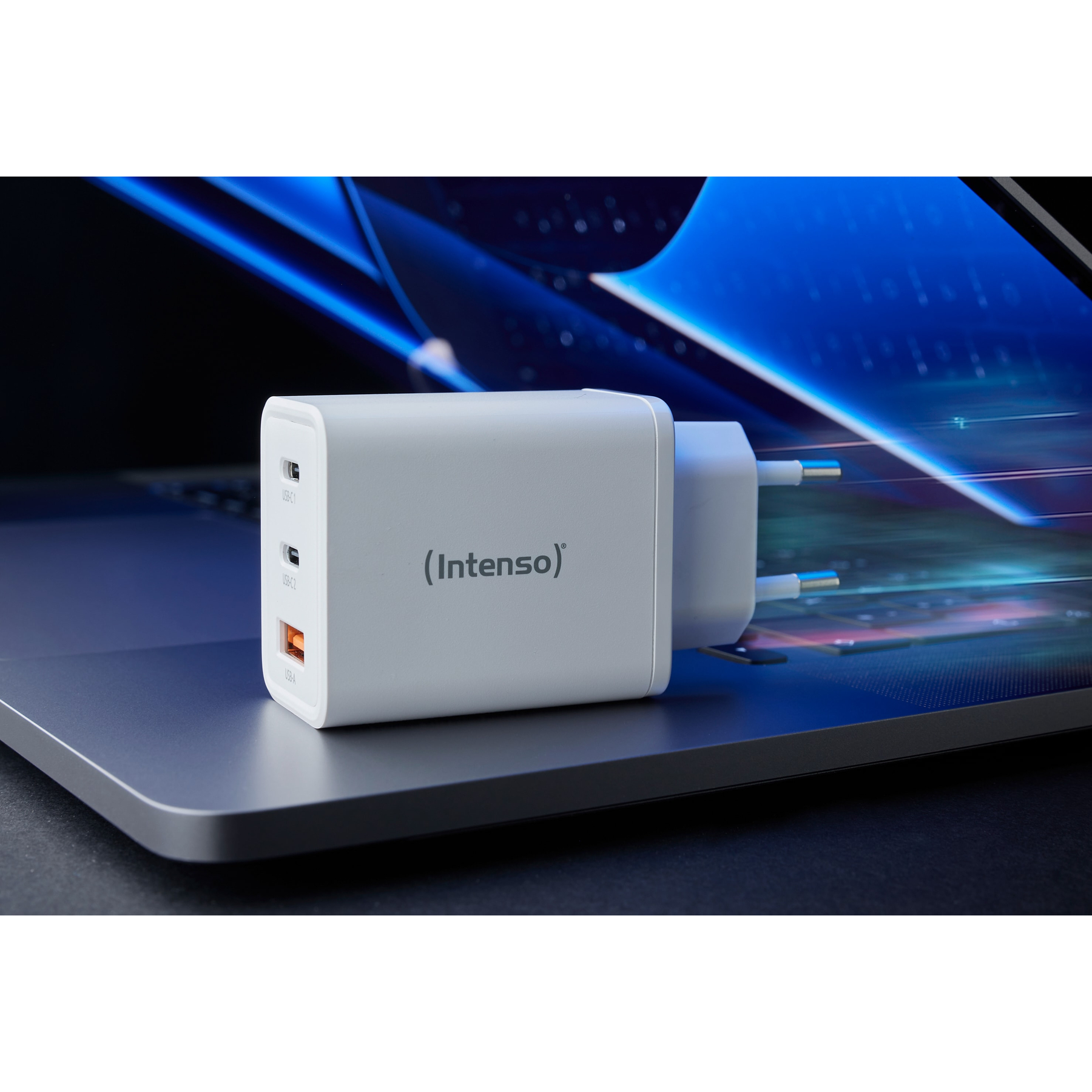 Un cargador blanco Intenso está sobre un portátil. Tiene múltiples puertos USB y un enchufe europeo. El fondo está borroso.