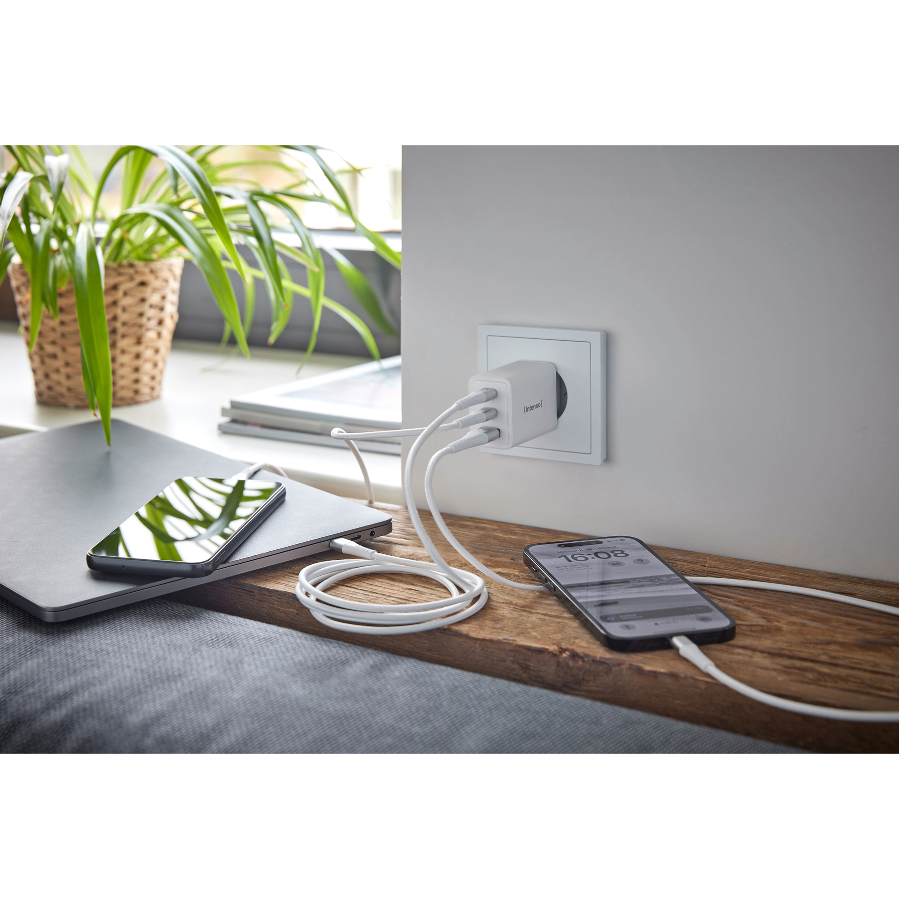 Una estación de carga con múltiples cables USB conectados a una toma de corriente. Teléfonos y un portátil están cerca.