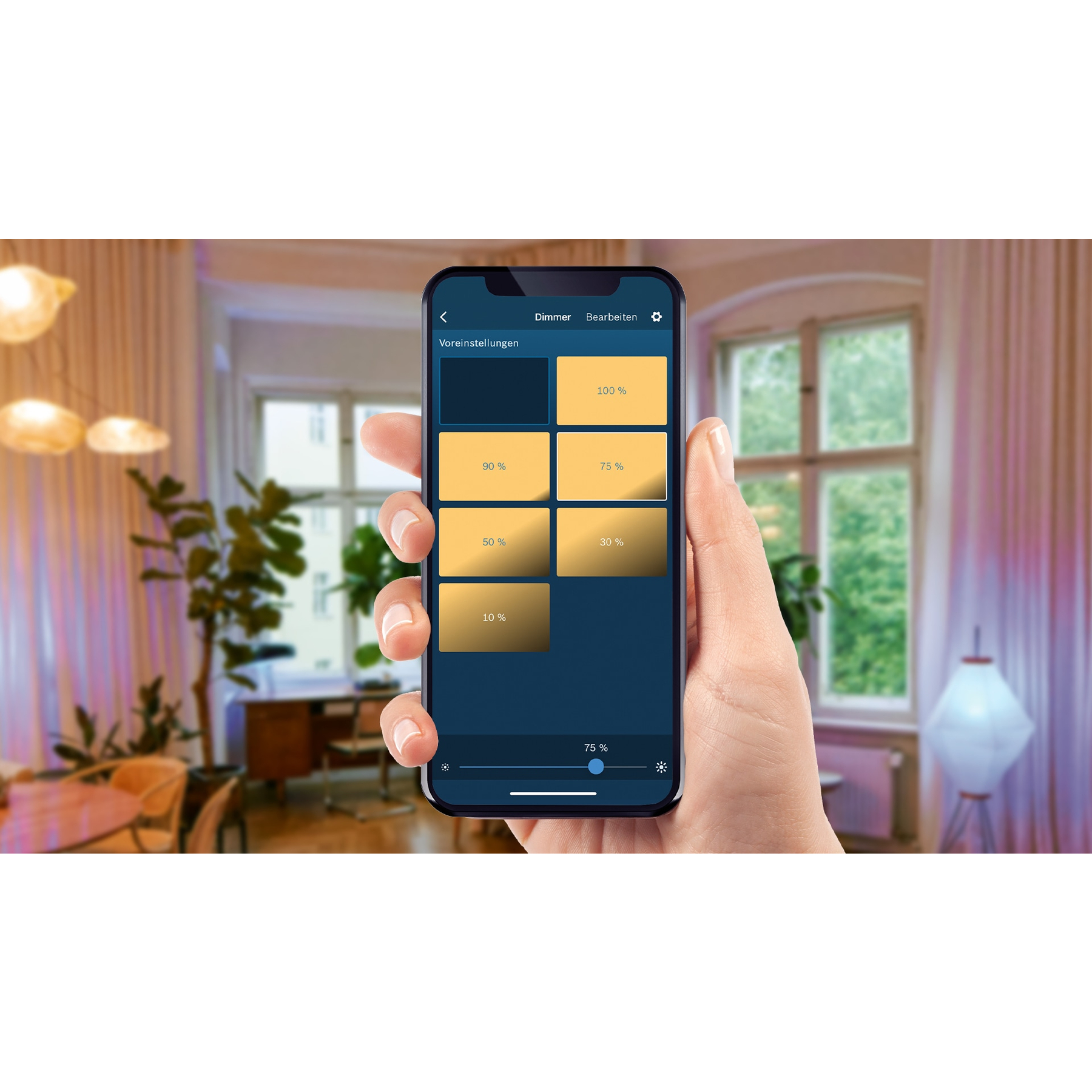Eine Hand hält ein Smartphone mit Dimmereinstellungen. Der Hintergrund ist ein Raum mit Fenster, Pflanzen und einer Lampe.